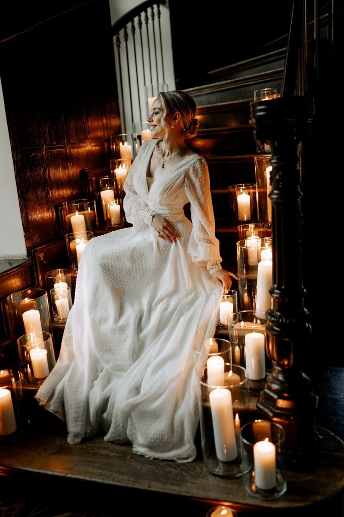 Junge Frau in weißem Kleid sitzt auf Kerzen-beleuchteter Treppe.