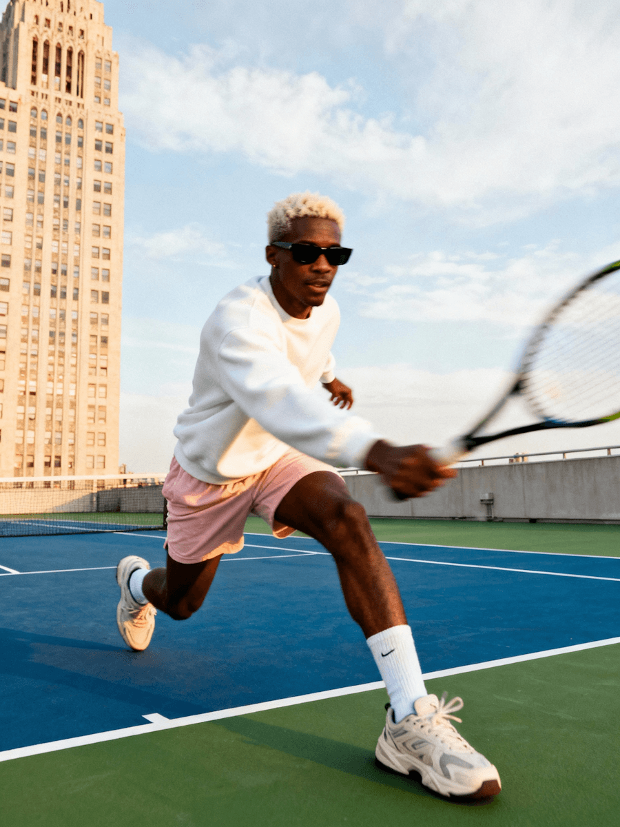 Man playing tennis on a rooftop court in New York City at golden hour