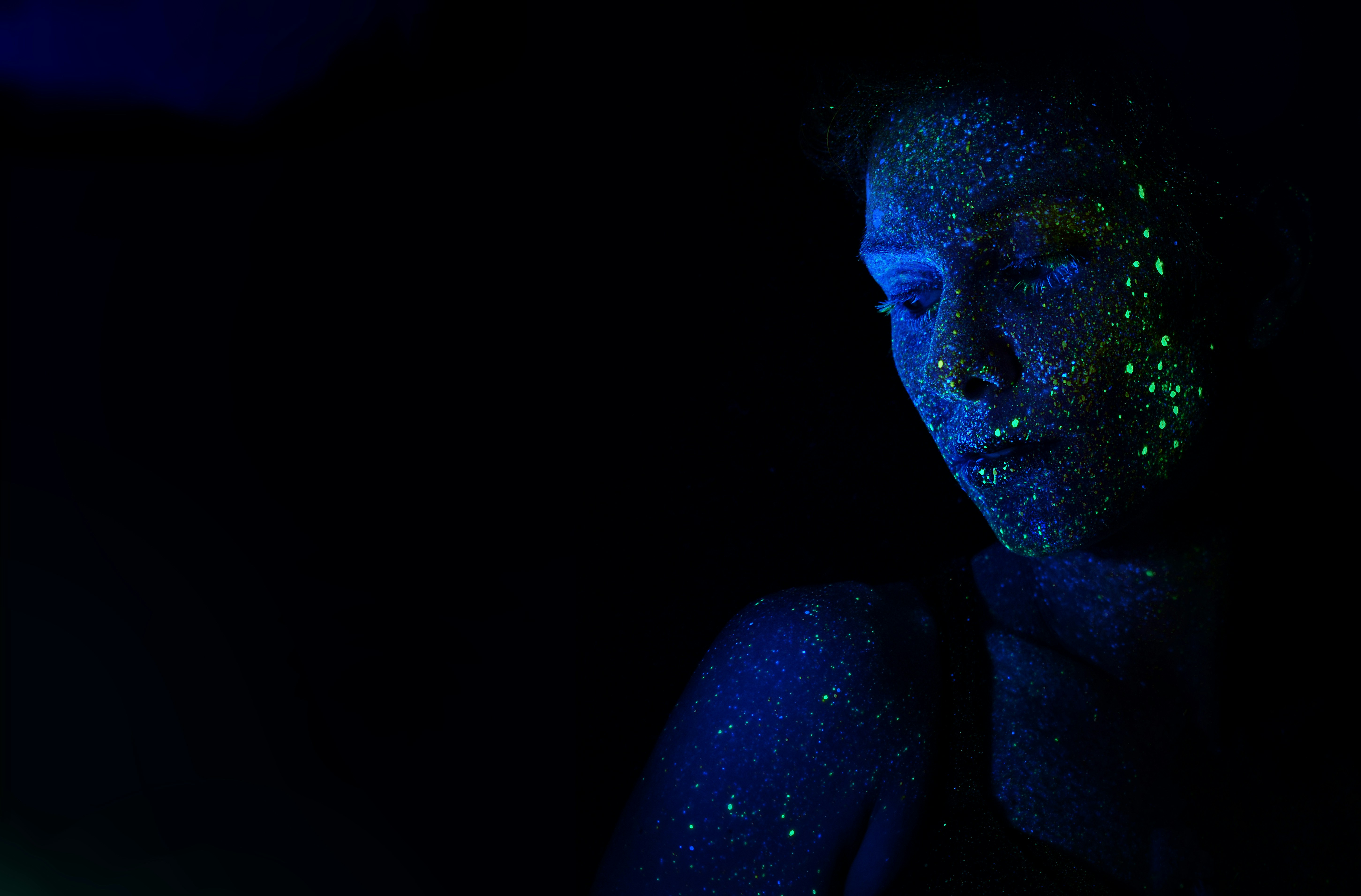 Portrait of a person with glowing paint under UV light in a dark environment