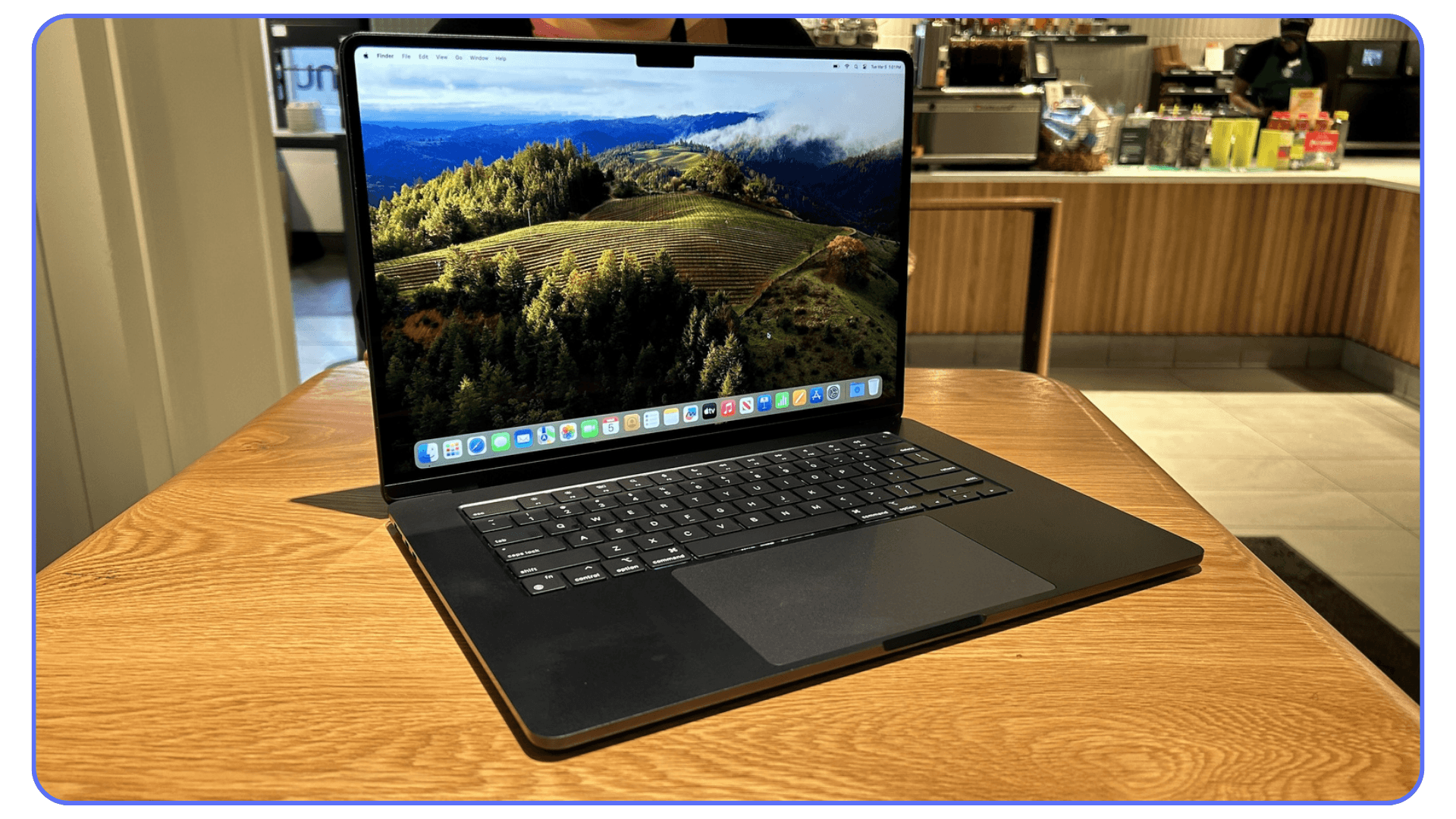An Apple MacBook Pro 14-inch with a mountain view displayed on its screen, placed on a table in a café with a warm, natural ambiance.