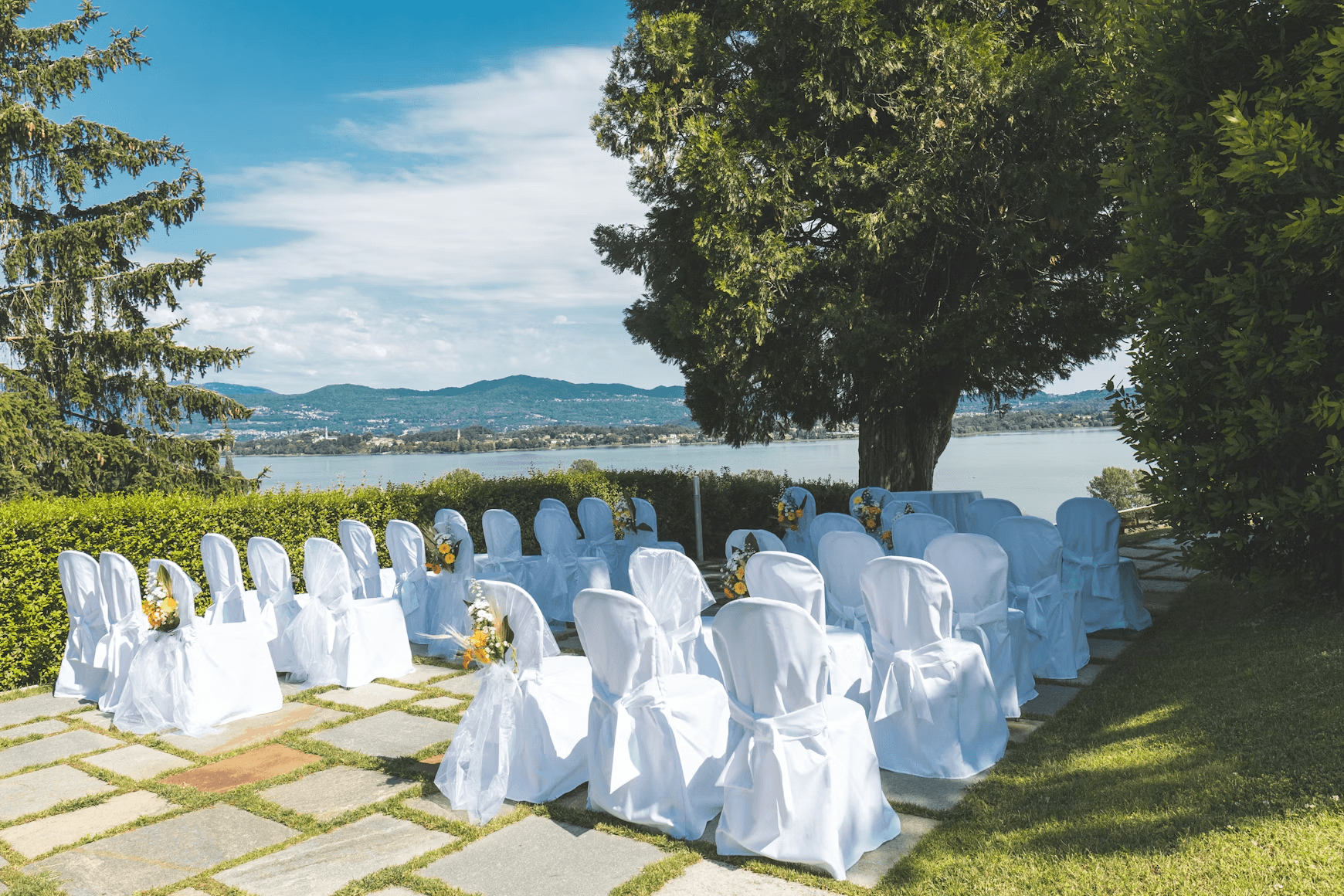 White chairs for wedding ceremony beside a tree
