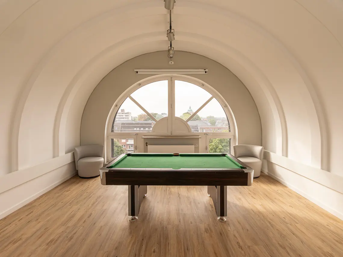 Billiards room in student accommodation in Münster with pool table and large arched window