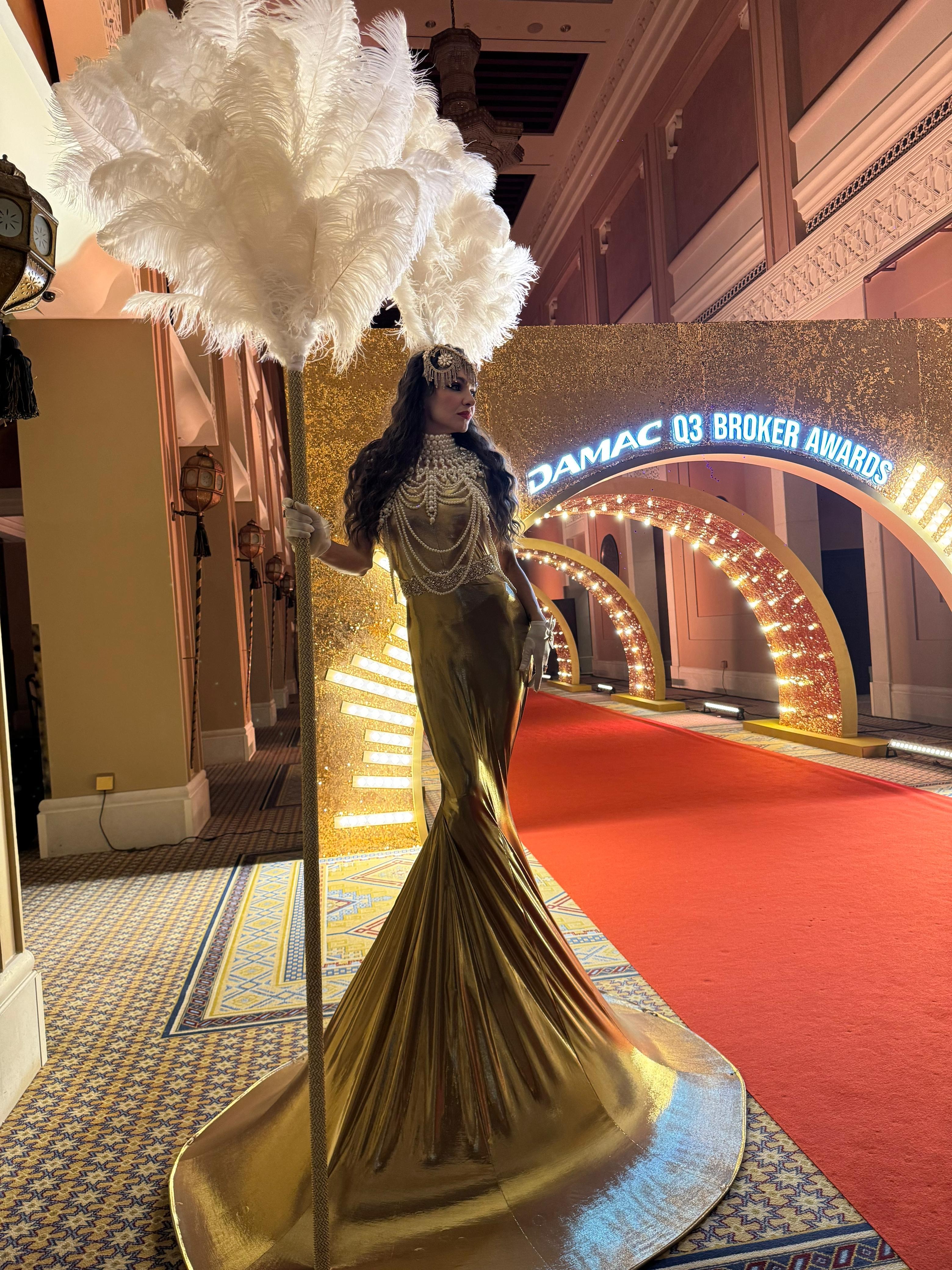 Gold stilt performer holding large white feather prop at DAMAC Q3 Broker Awards red carpet