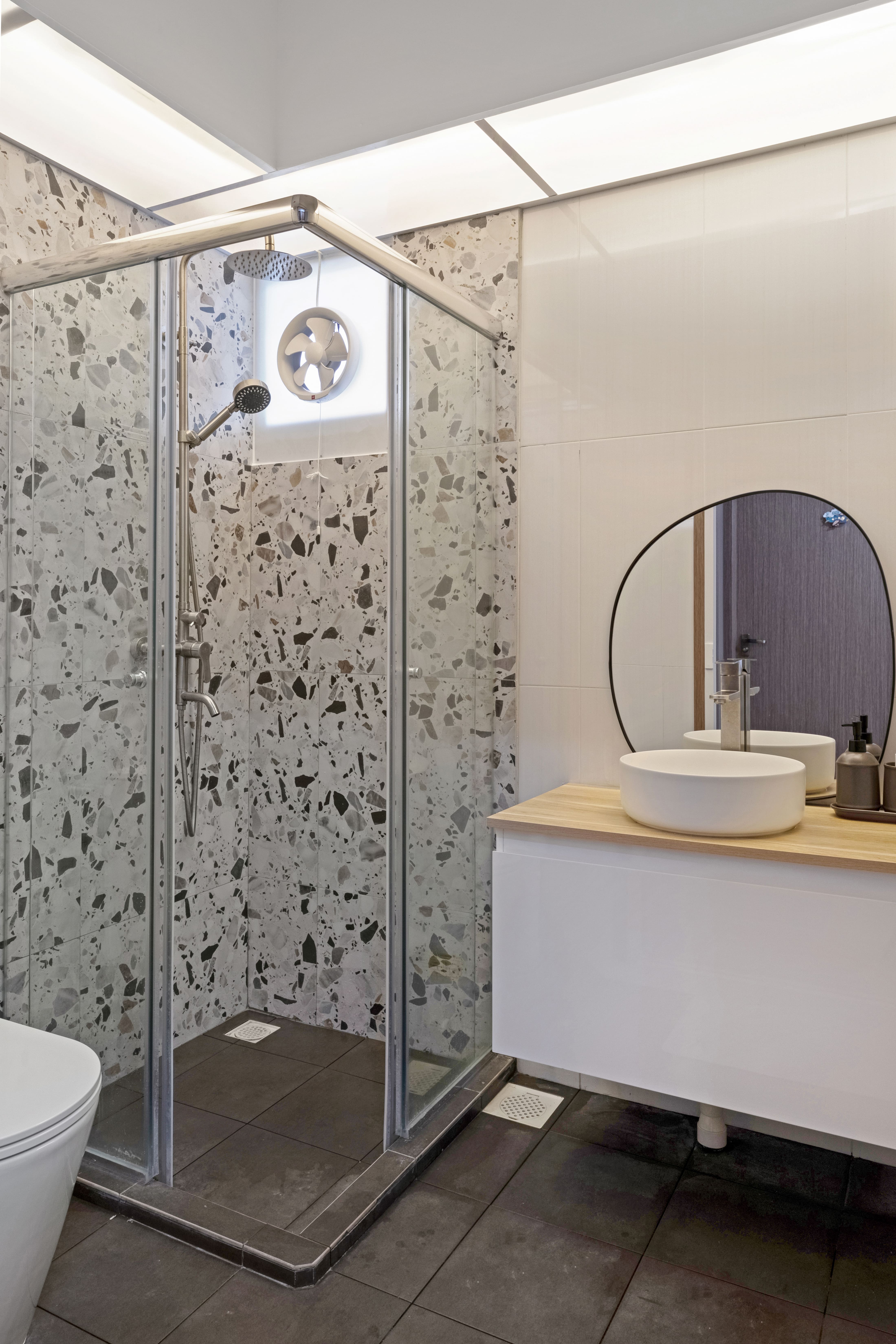A modern bathroom with terrazzo-tiled shower walls, a frameless glass enclosure, and a sleek vanity topped with a round vessel sink and minimalist mirror.