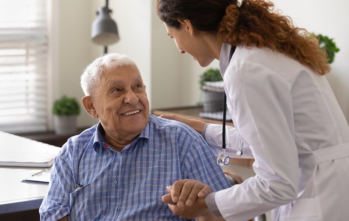 Female Healthcare Worker holding the hand of an older man, smiling