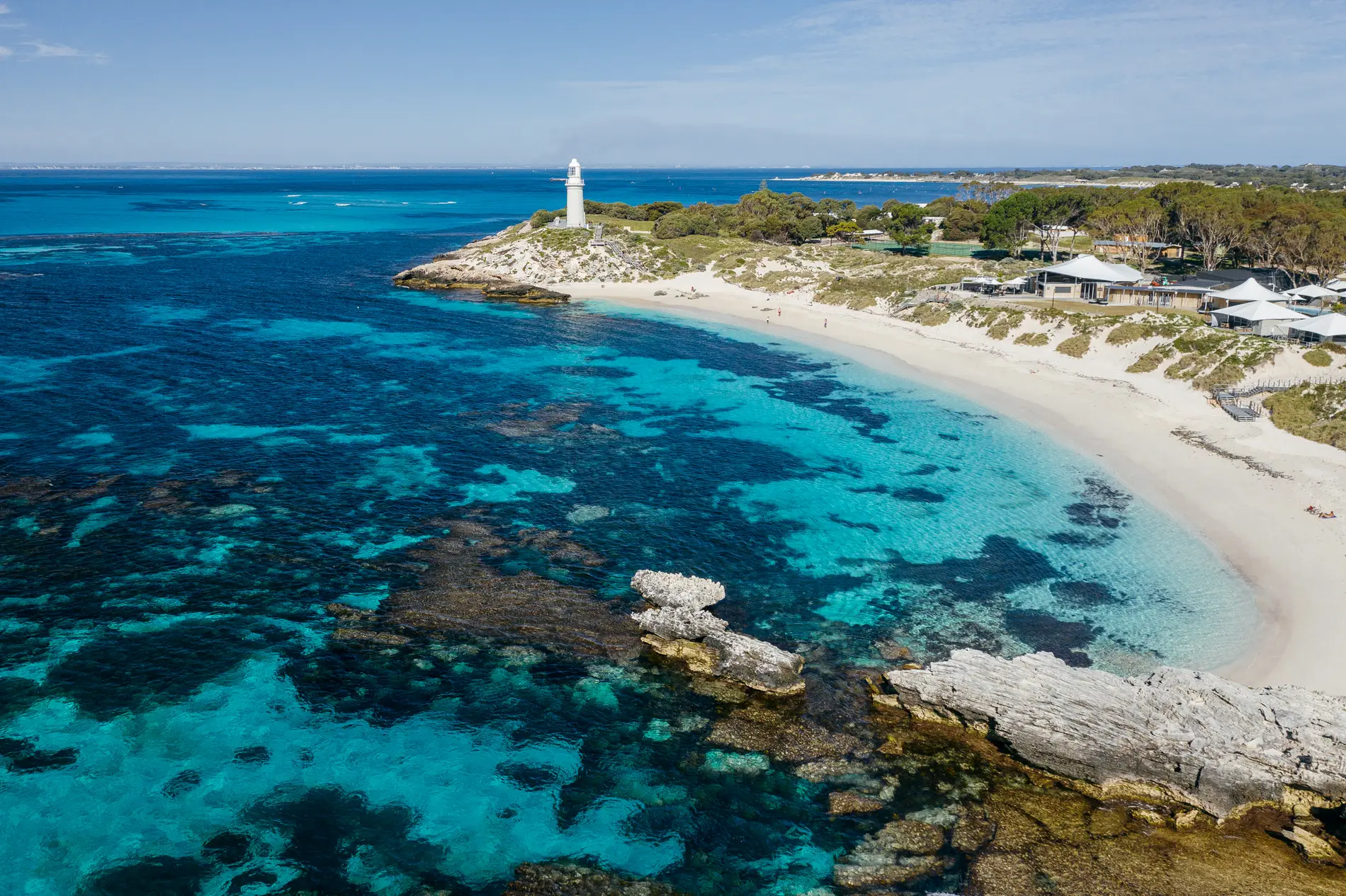 Aerial of a lighthouse on a low point above reef and clear blue water