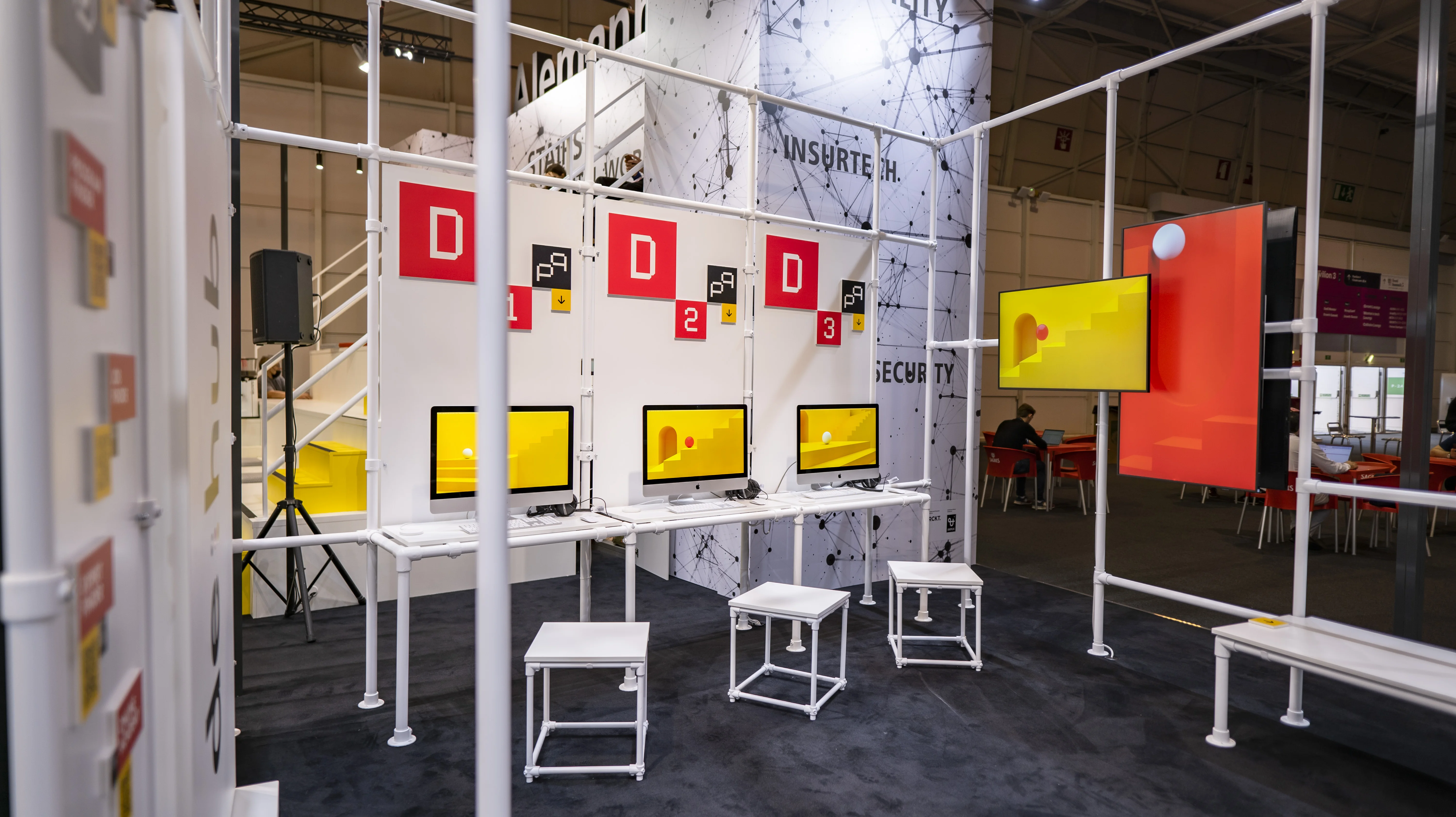 Demo stations with screens and white stools in the open frame architecture of the German Pavilion at Web Summit.