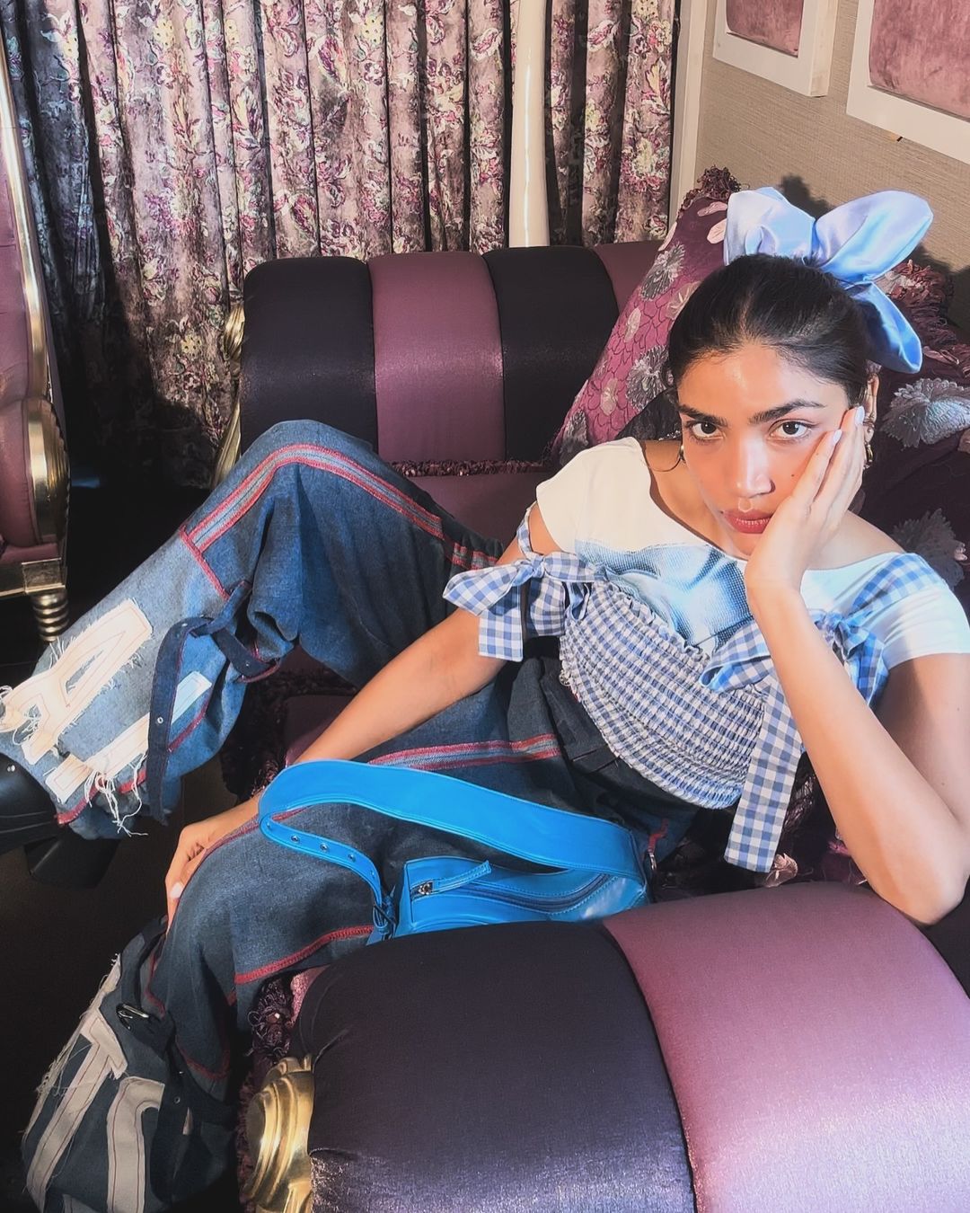 Instagram creator Pragya Beriwala in denim and a blue bow sitting on the sofa