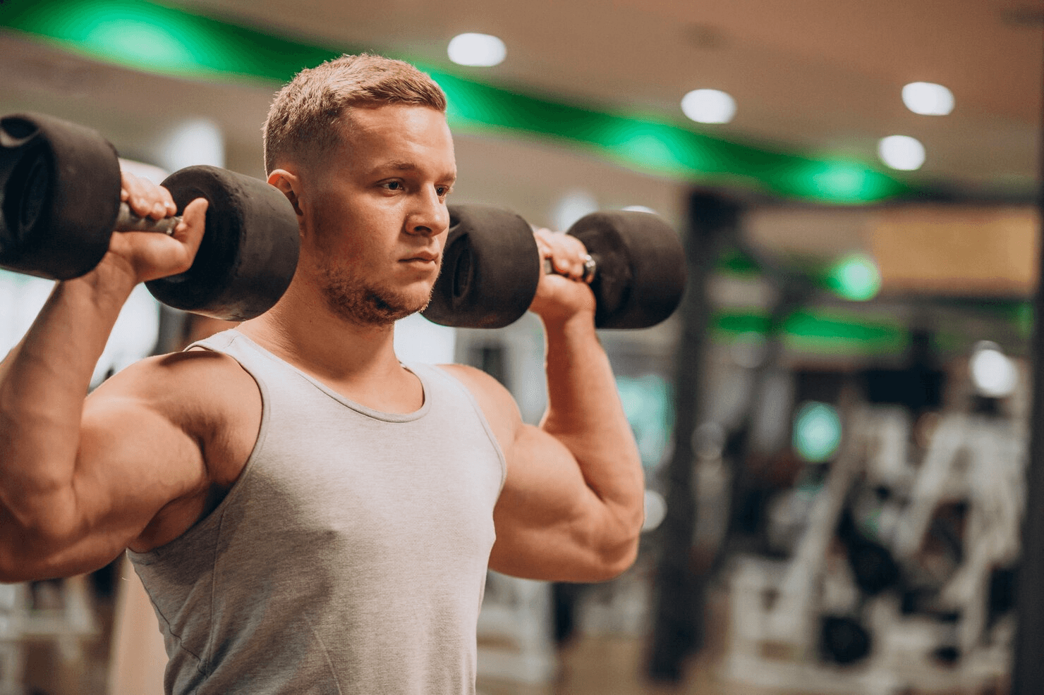 Man lifting a dumbbell on his shoulder in a gym.