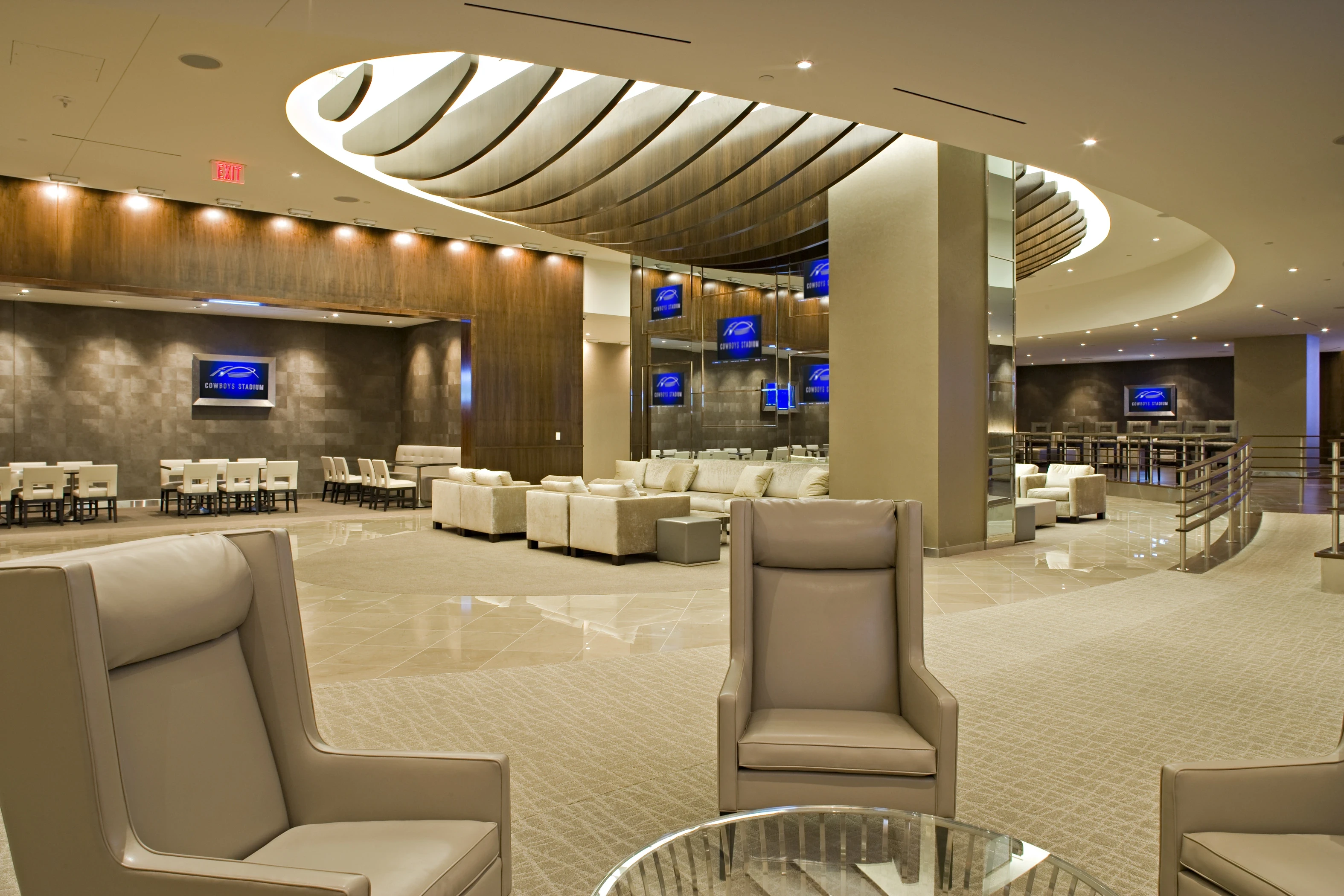 Luxury stadium suite lounge with curved ceiling design, upscale seating, dining tables, and large screens displaying event branding.
