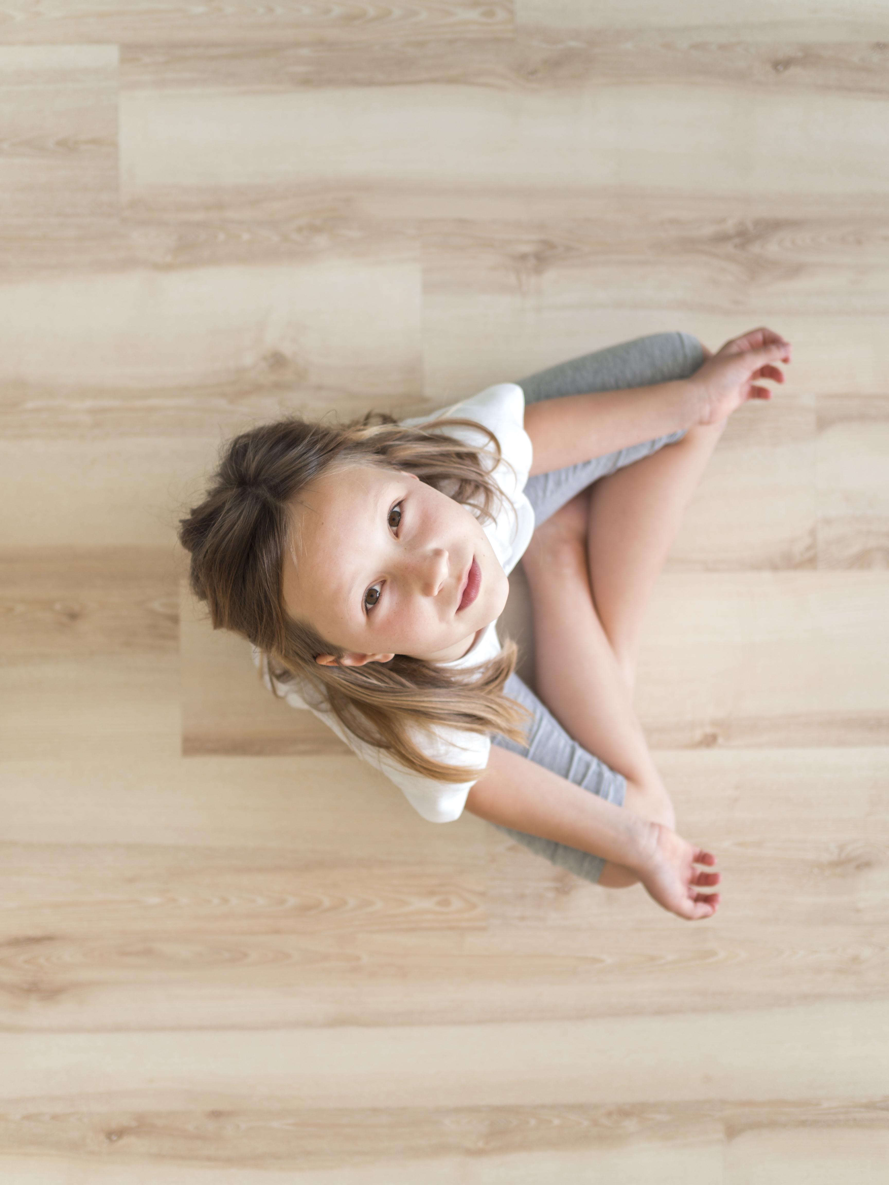 Child sitting comfortably on smooth timber-look flooring, showing a safe, warm surface designed for everyday family life.