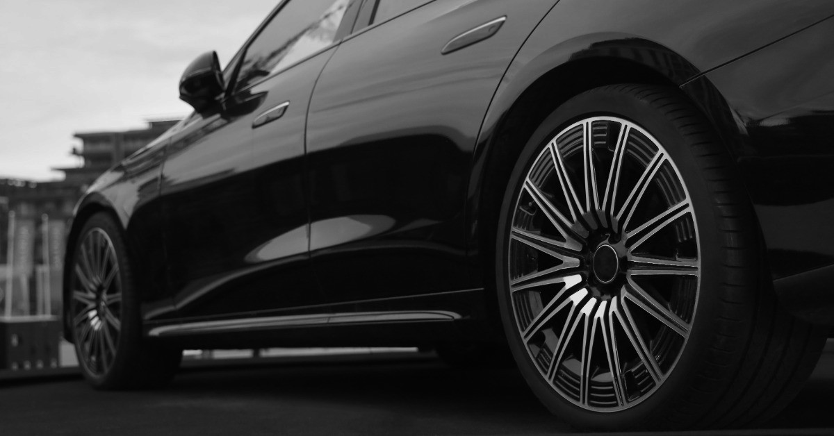 A ground-level view from the rear driver side of a black car. The vehicle is parked outside on a dark asphalt.