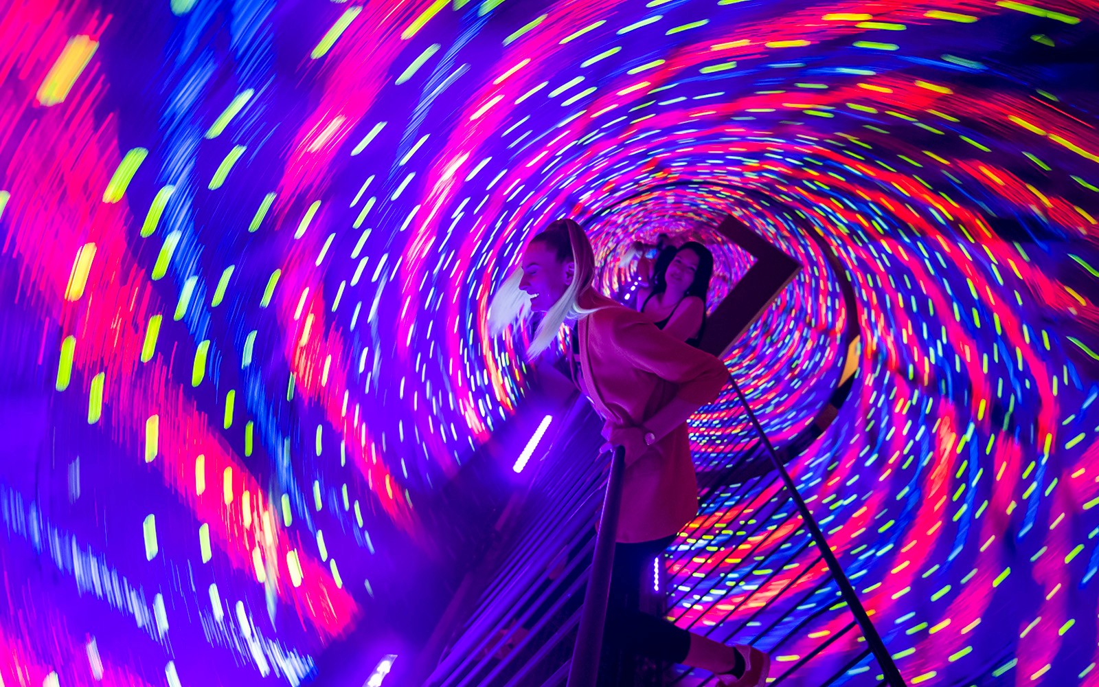 Visitors experiencing a colorful vortex tunnel with swirling lights.