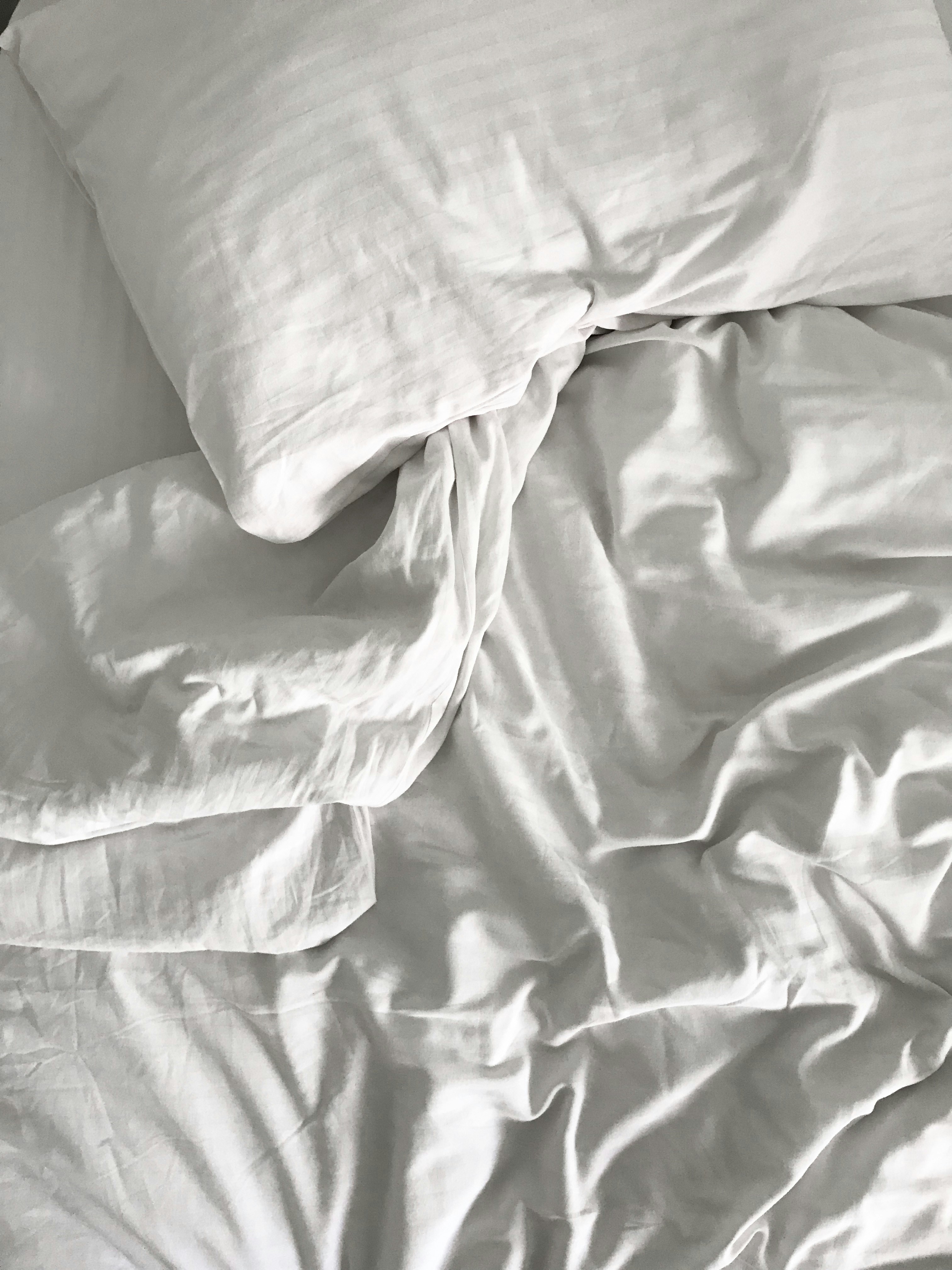 A close-up view of crumpled white bedding with pillows and sheets arranged in a casual, unmade state.