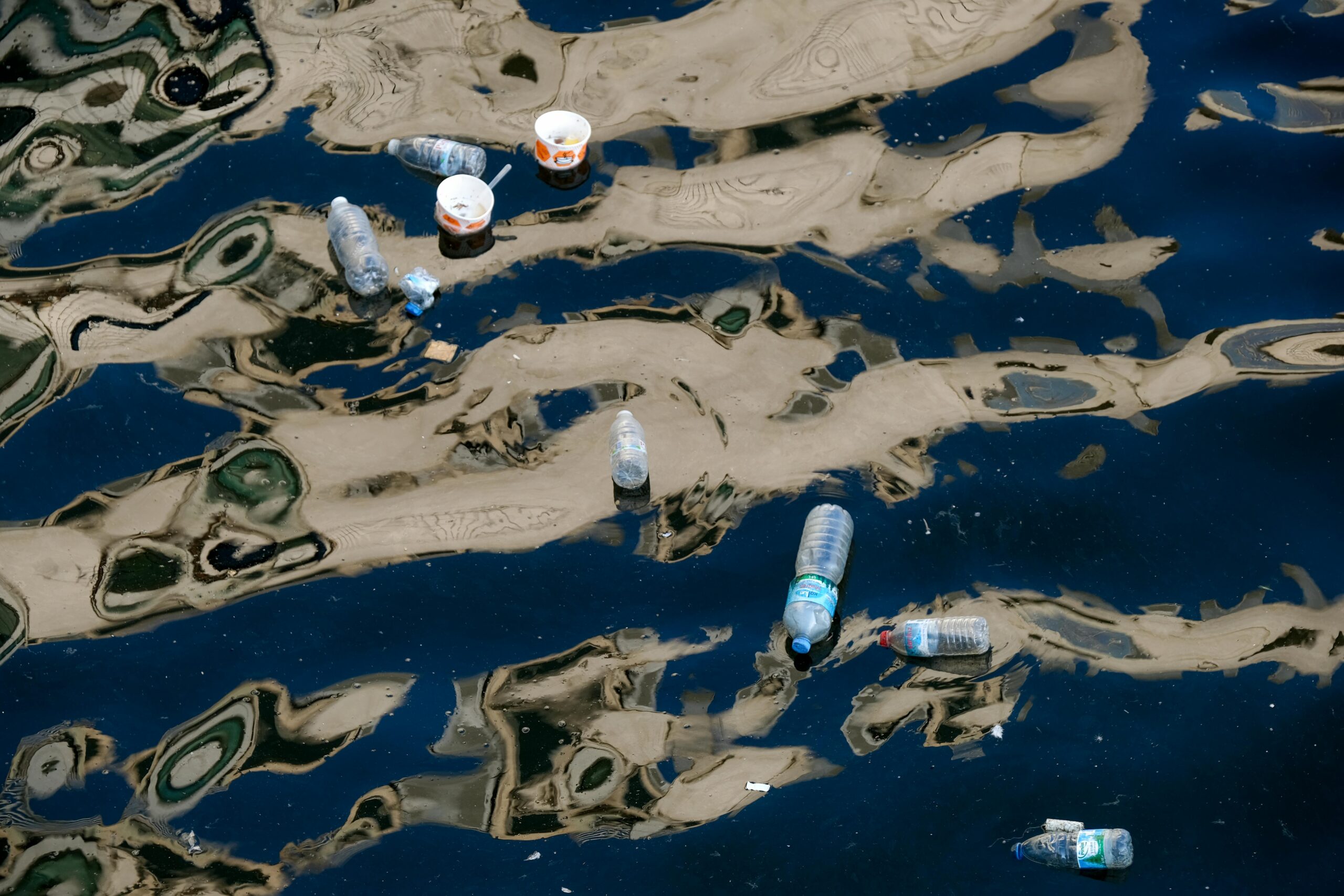 Plastikowe odpady, w tym butelki i kubki, unoszące się na zanieczyszczonej powierzchni wody.