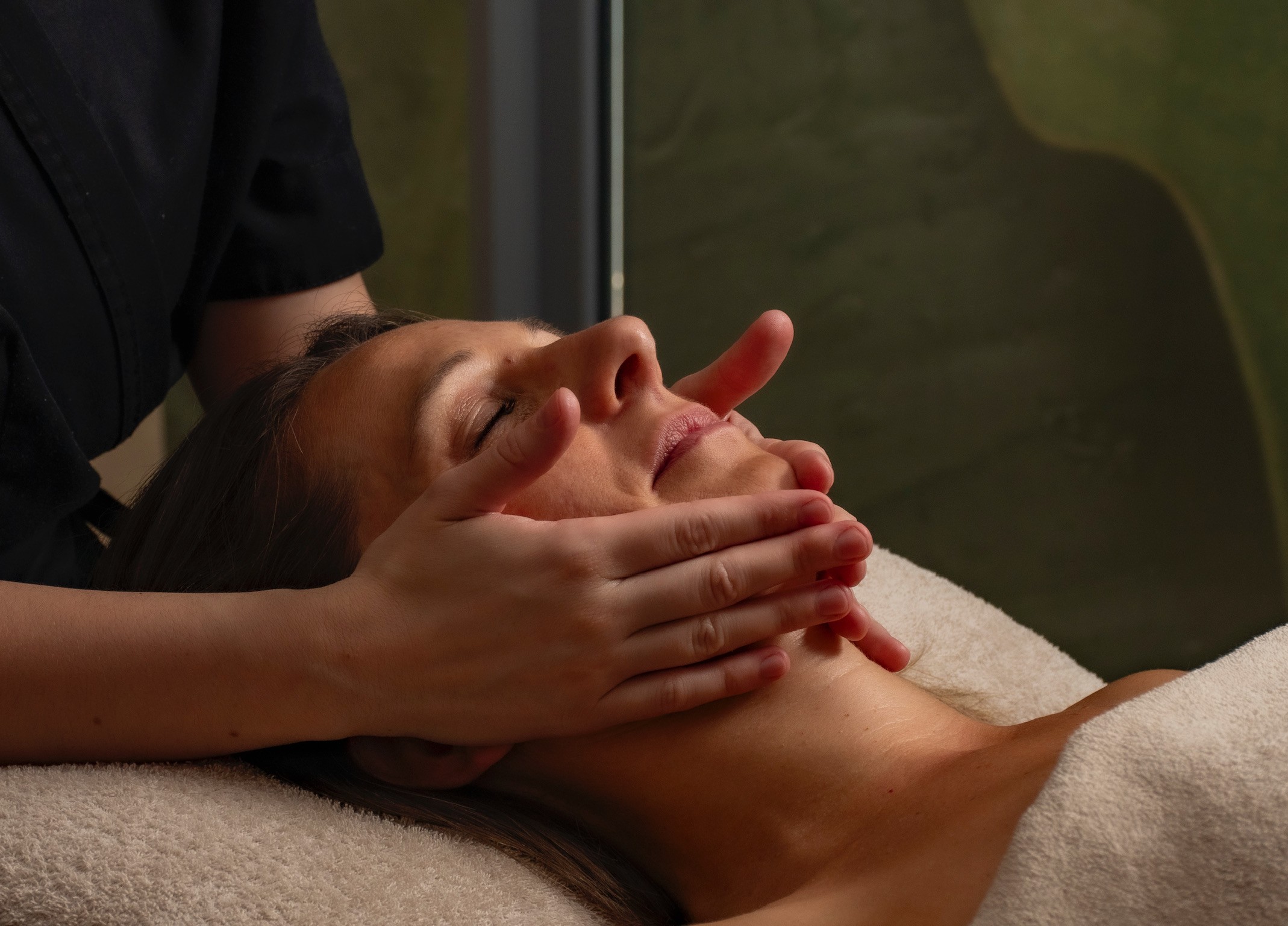 Femme recevant un massage du visage dans un spa, moment de détente et de bien-être.