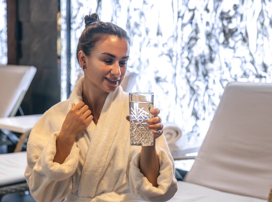 woman drinking water after a session of how long to sit in sauna after workout to lose weight to stay hydrated