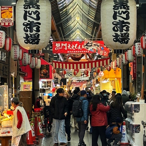 繁忙的日本市场街道，两侧有各种商店，悬挂着大型灯笼，人们在步行和购物。