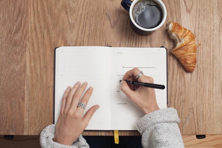 A woman planning her day on her journal while drinking coffee