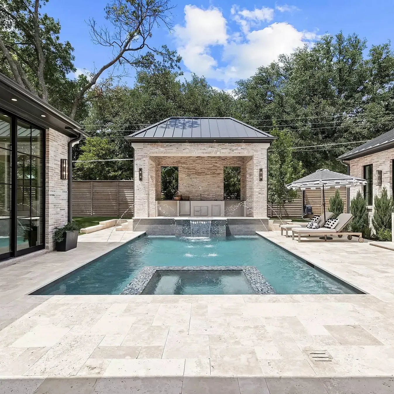 An outdoor pool area with a luxurious house and surrounding greenery.