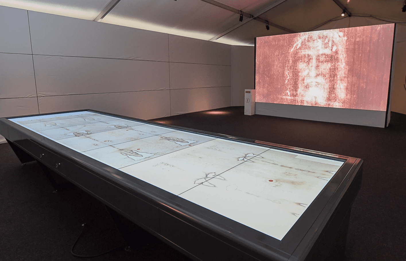 L'interno del padiglione con il tavolo interattivo della Sindone in primo piano e il video emozionale sullo sfondo 