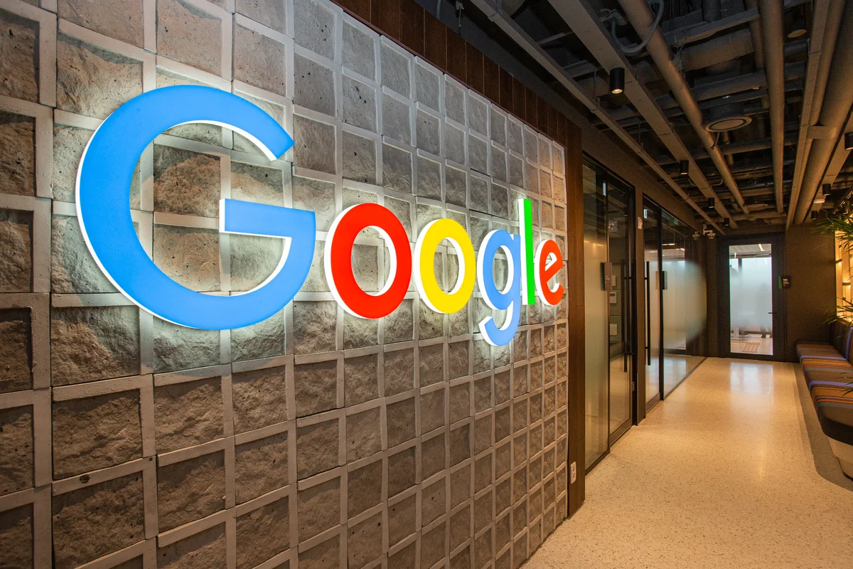 A colorful Google logo, illuminated in a neon-like glow, is prominently displayed in the interior of a modern office building.