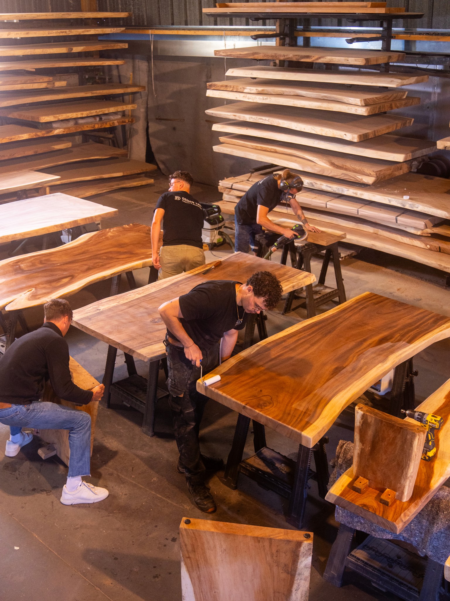 Artisans travaillant des plateaux de tables en bois massif dans un atelier de menuiserie.