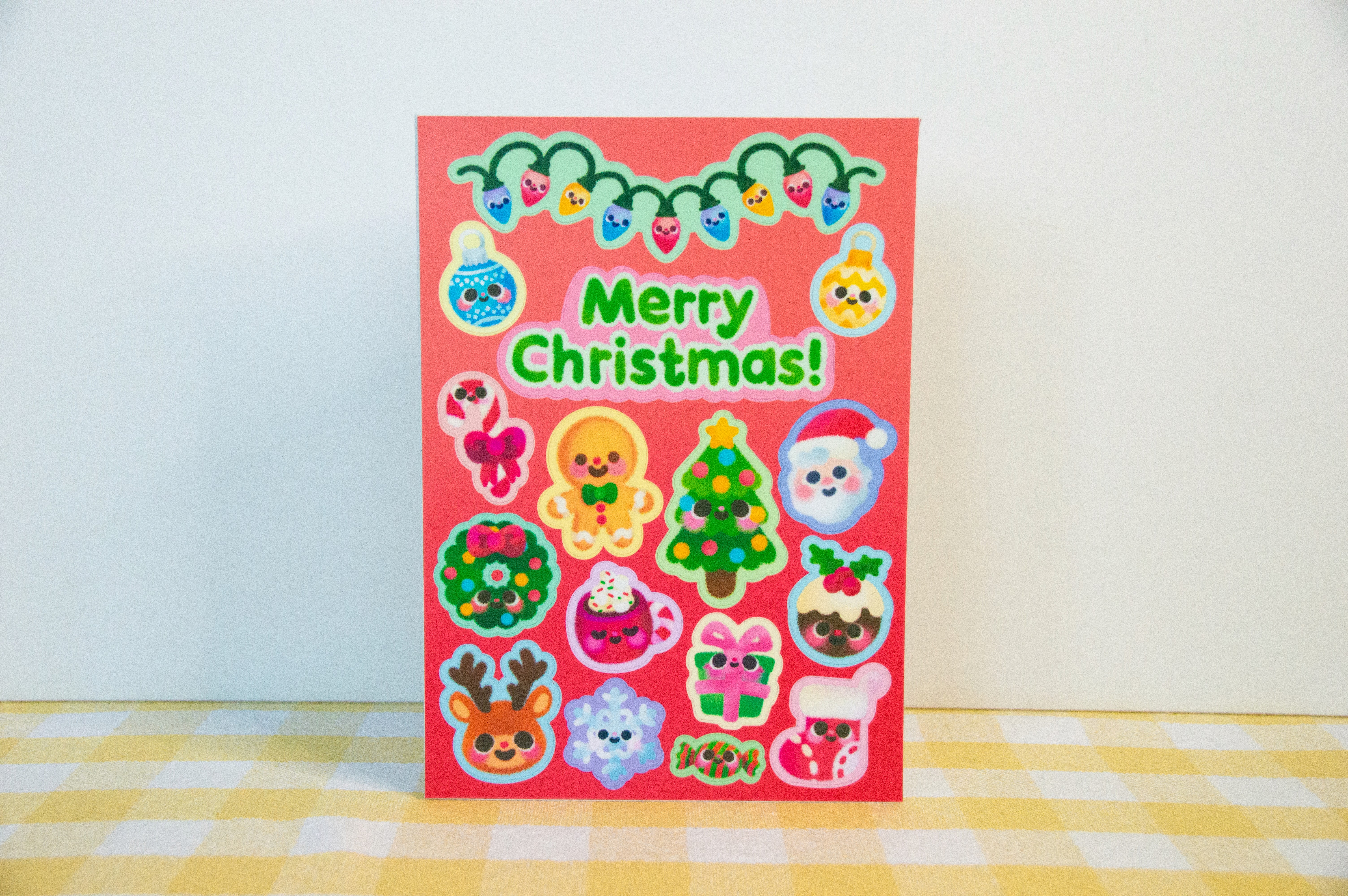 A red Christmas card that is also a sticker sheet. There are many stickers, including a Christmas tree, Father Christmas, a reindeer, a present, and sweets.