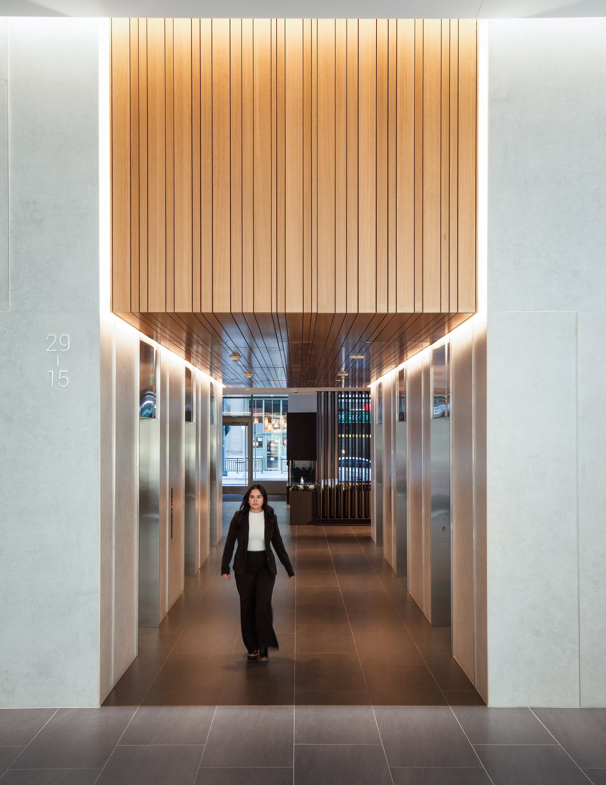 Woman in suit walks down wood-paneled elevator lobby hallway.