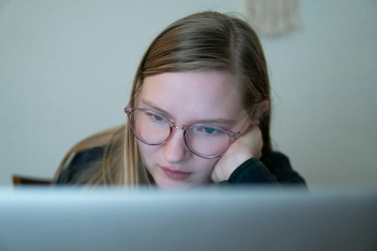 A woman with glasses concentrating on a laptop screen.