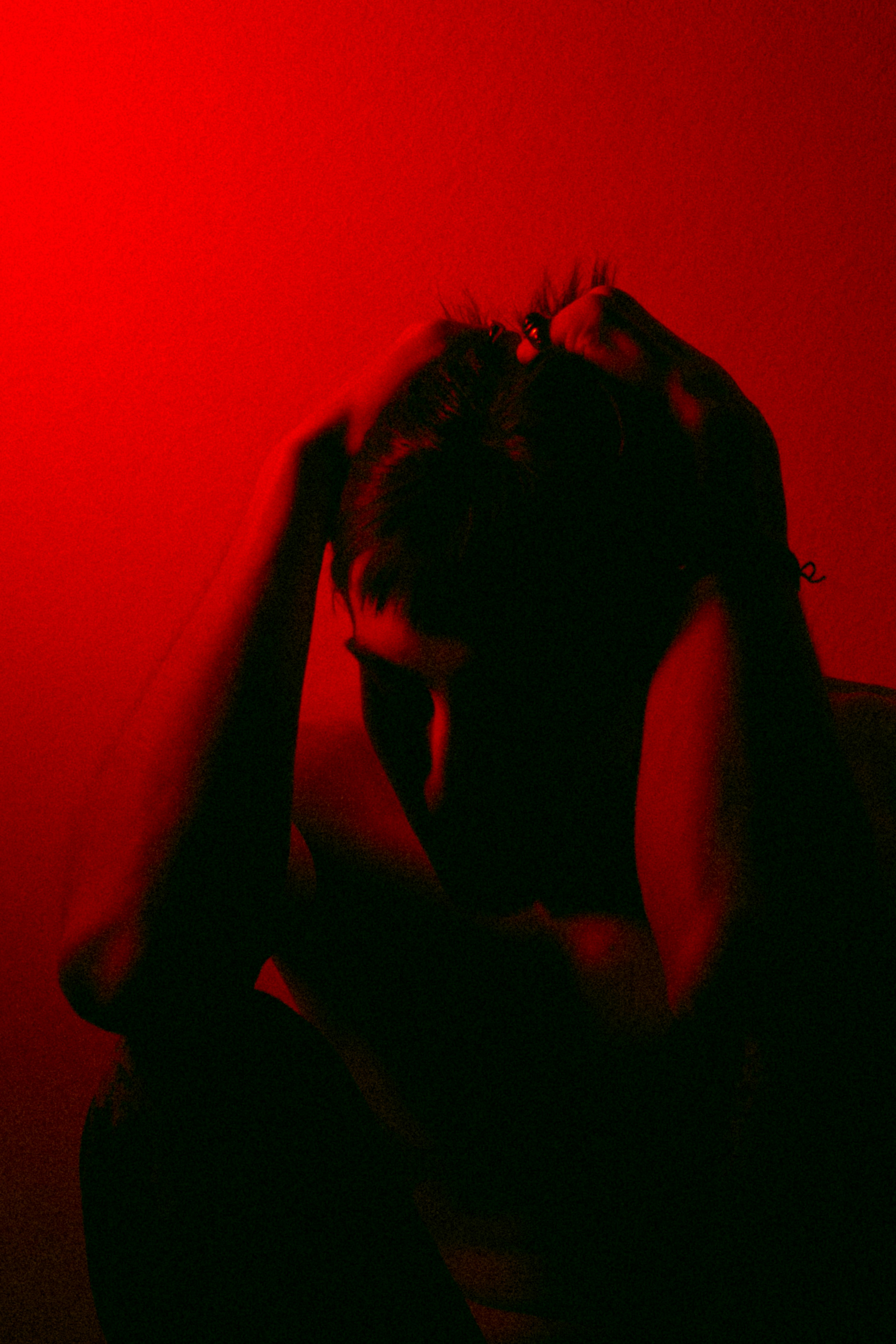 young man under red light axiously crouching with his hands on his head