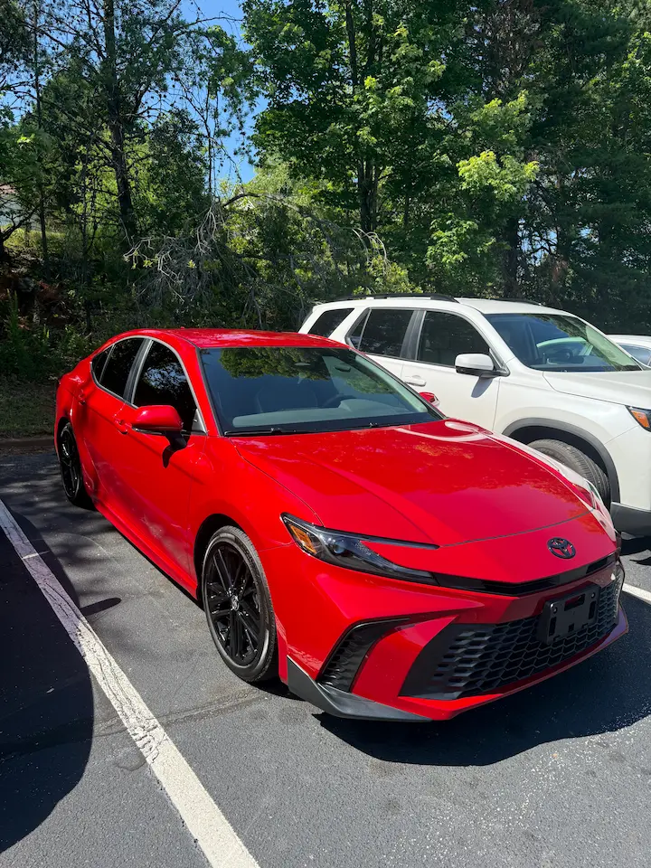 A red Camry Hybrid parked outside, representing a difficult but necessary decision to buy a reliable vehicle while facing uncertain health, work, and financial circumstances.