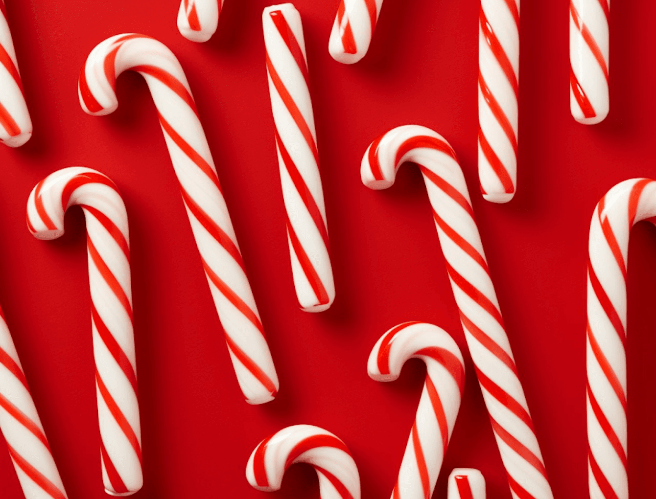 A collection of colorful candy canes arranged neatly on a vibrant red background.