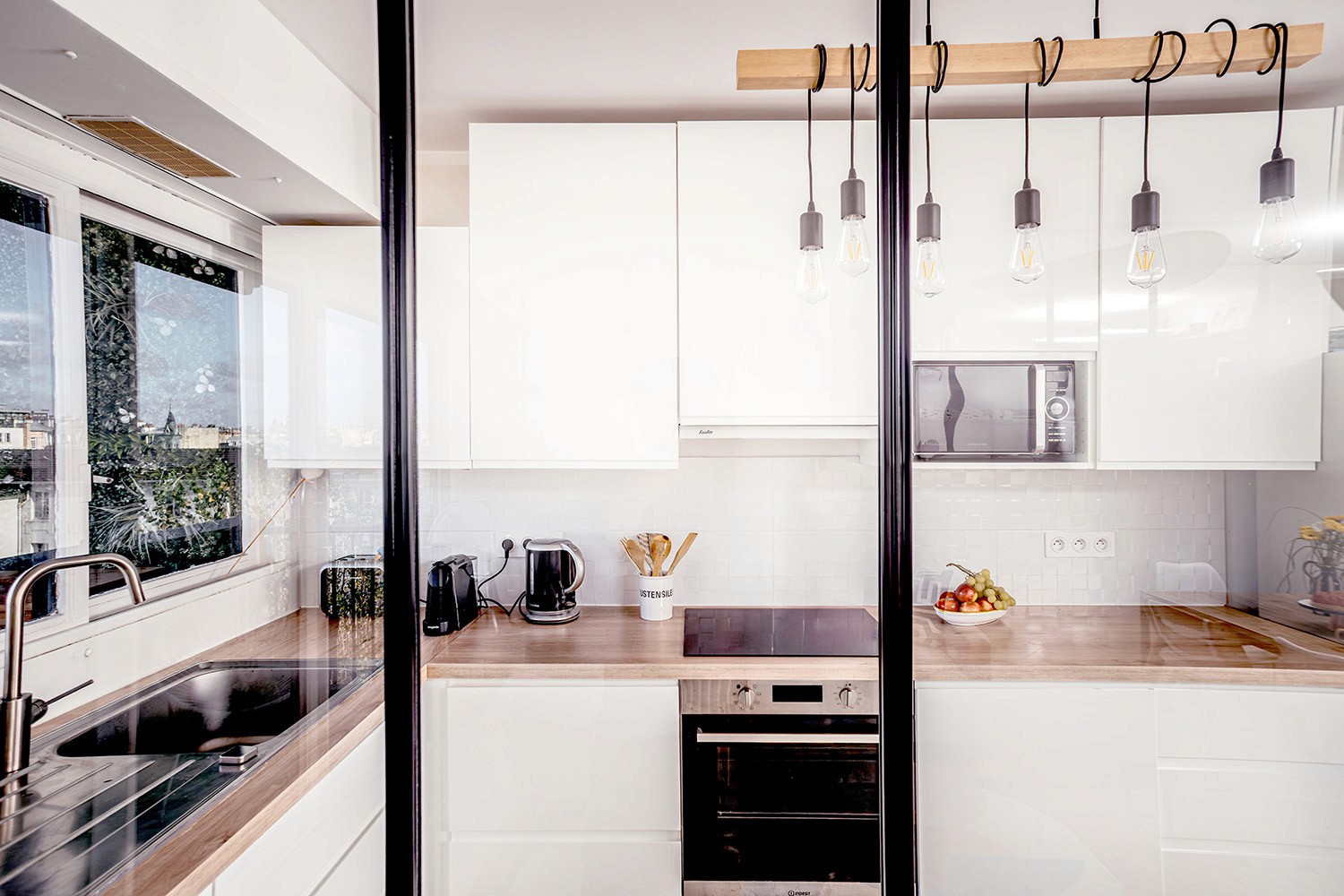 Cuisine ouverte derrière verrière atelier noire dans un appartement rénové.