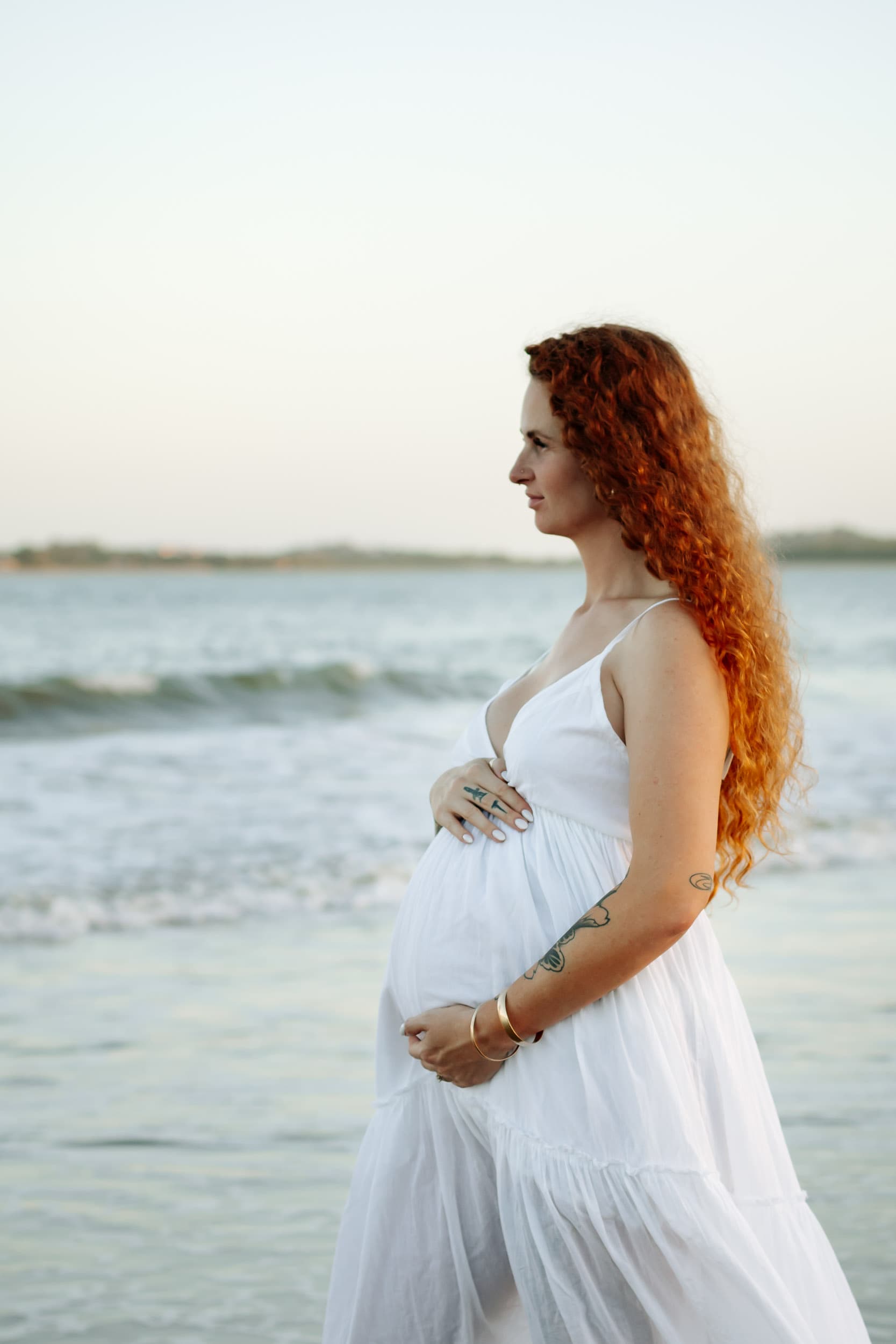 Dreamy beach maternity photograph in Mackay featuring an expecting mother framed by pastel skies at dusk.
