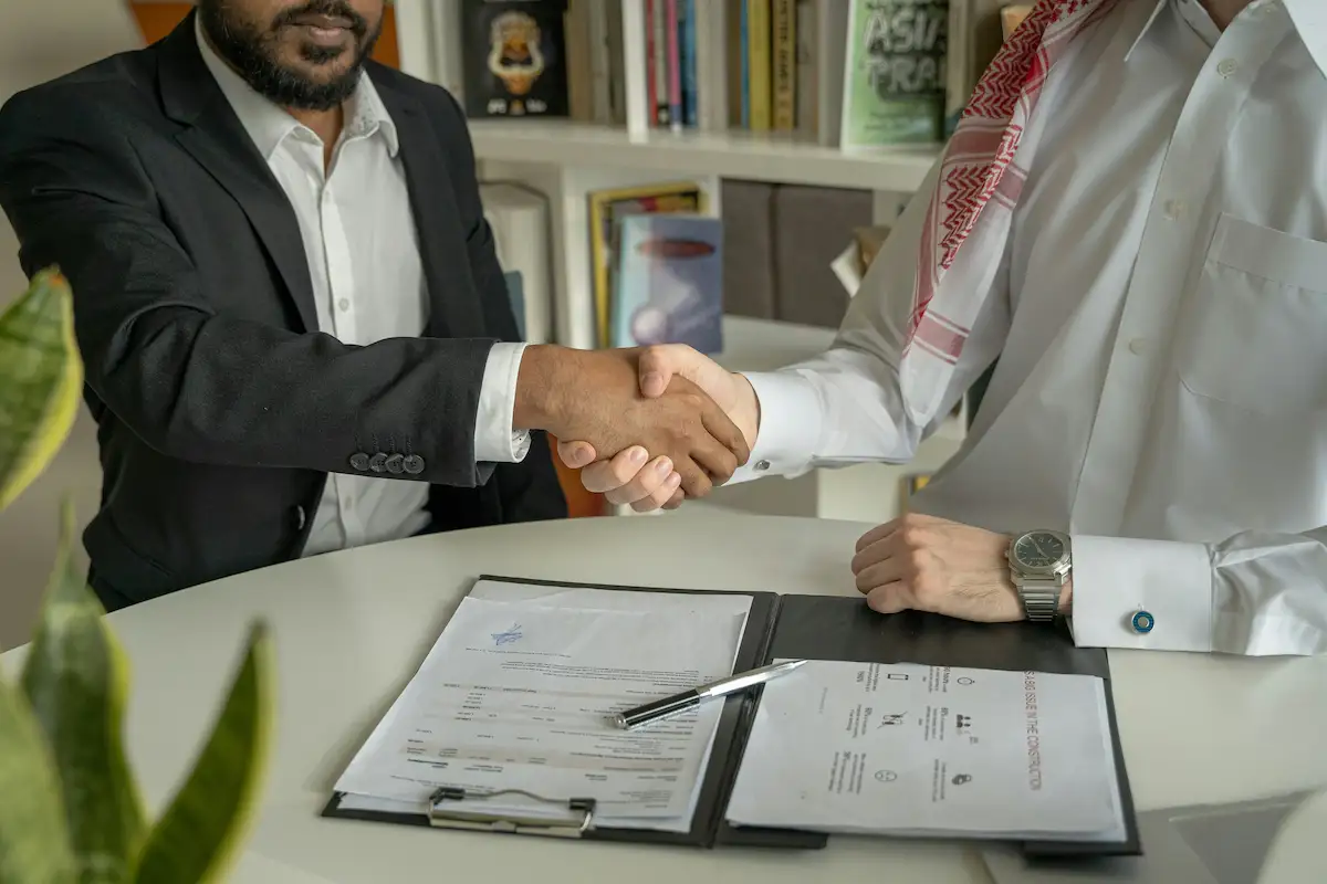 A couple of men shaking hands over a desk.