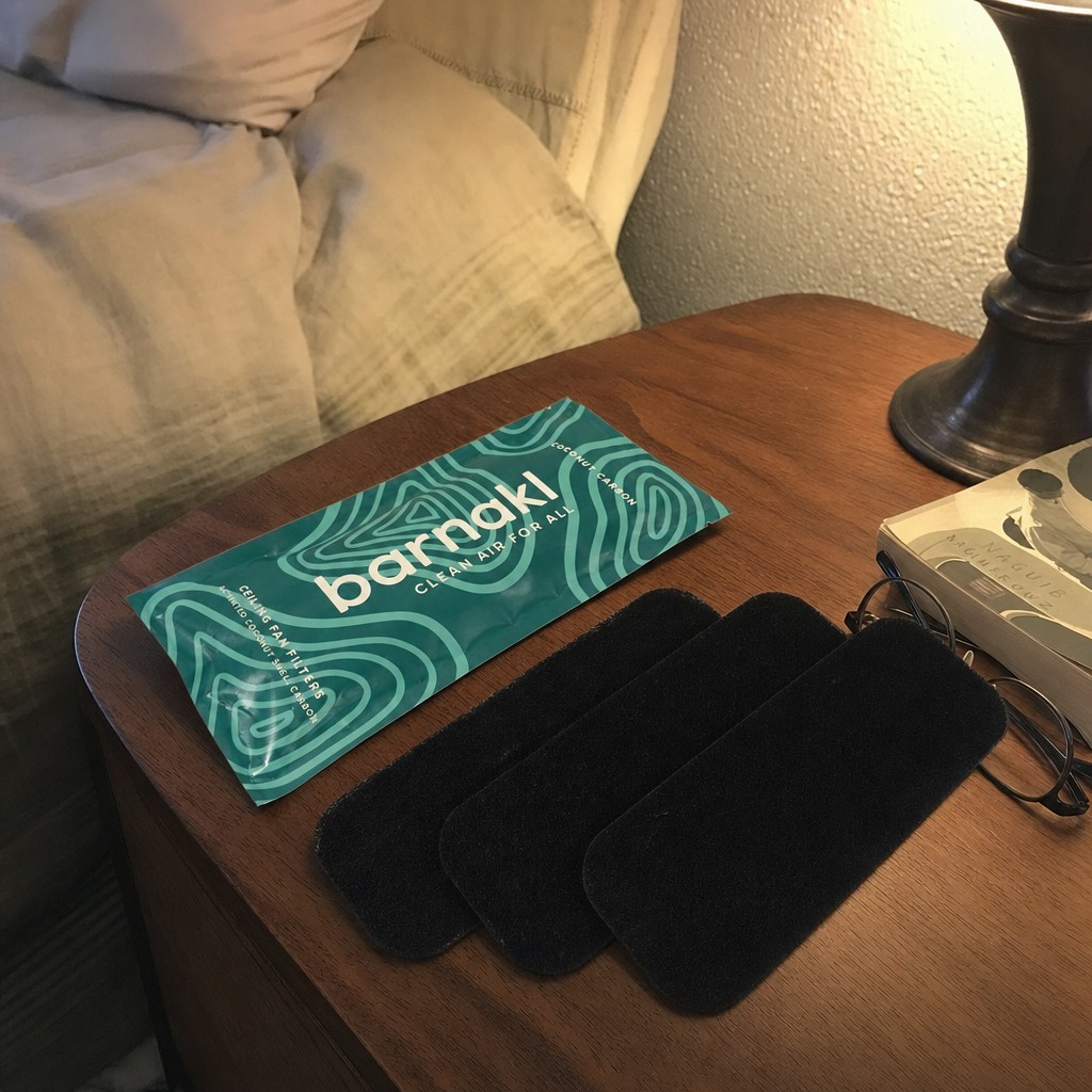 The Barnakl pouch and three matte black filter pads on a bedside table at night.