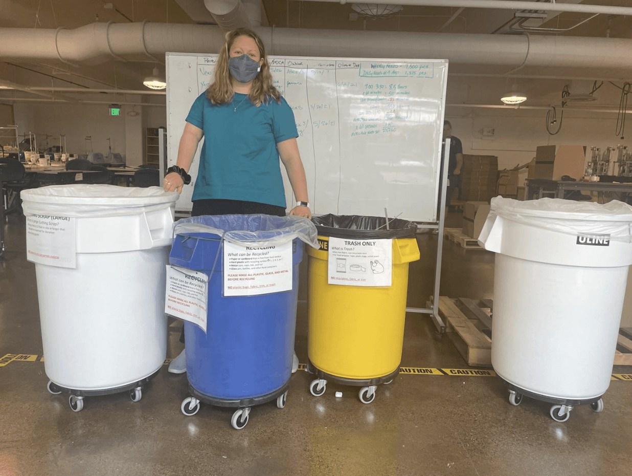 A person stands in front of colorful bins on wheels, with a whiteboard in the background.