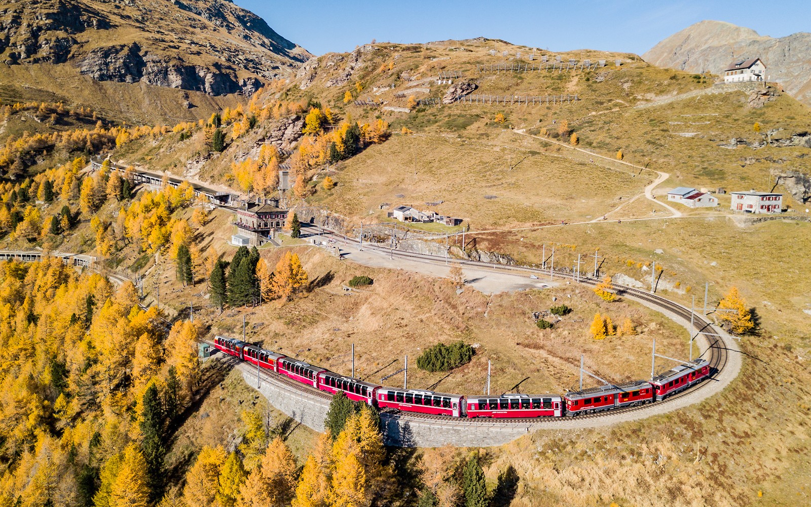 Bergtåg på kurvig bana vid Jungfraujoch järnvägsstation mitt i höstlandskap.