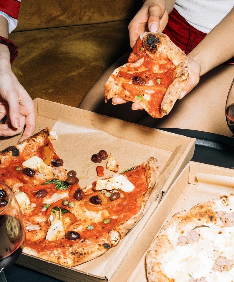 Close-up lifestyle photography of friends sharing slices from a Sauza Pizzeria box.