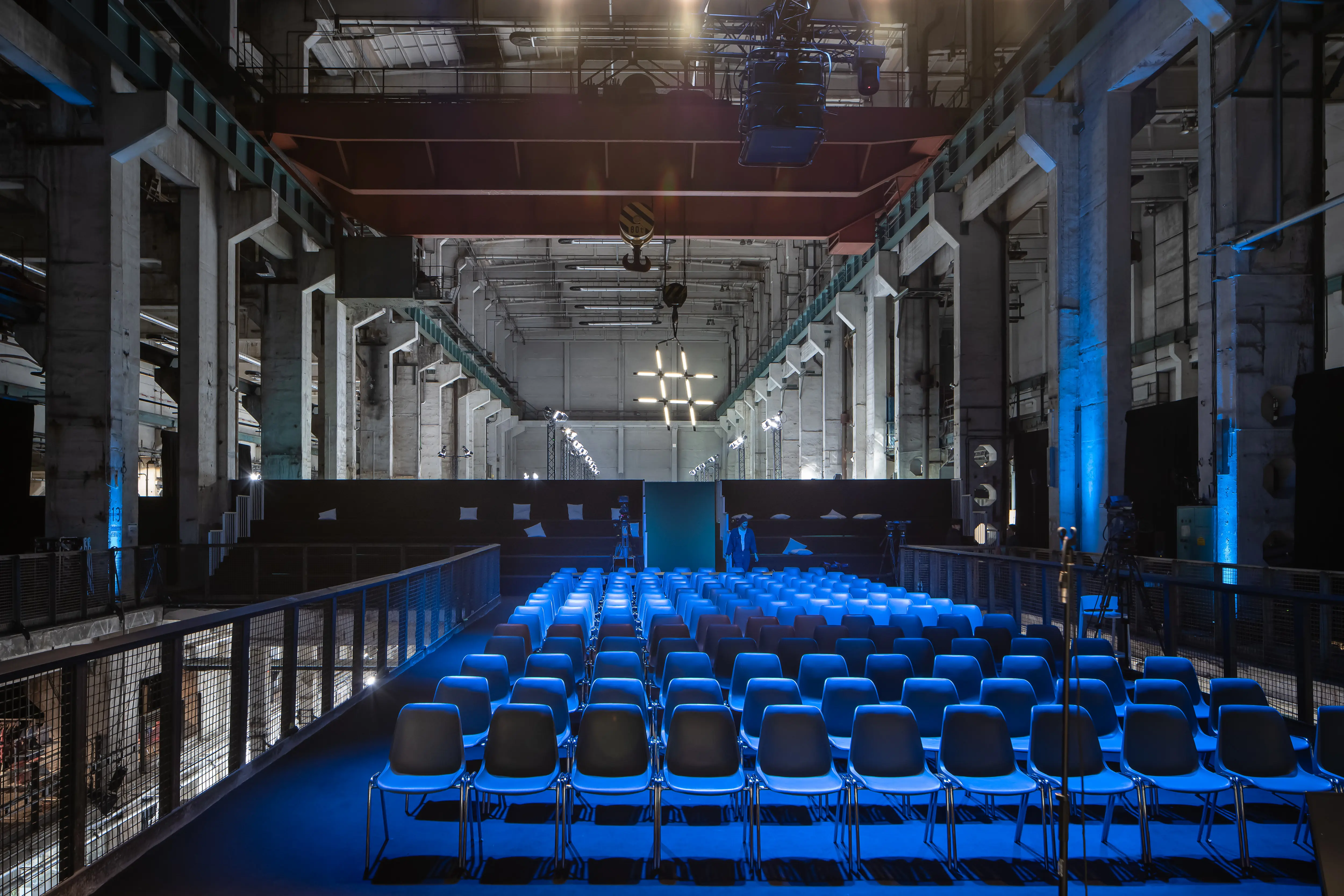 Rows of blue-lit chairs facing the Fashionsustain conference stage with a cross-shaped light installation at NEONYT.