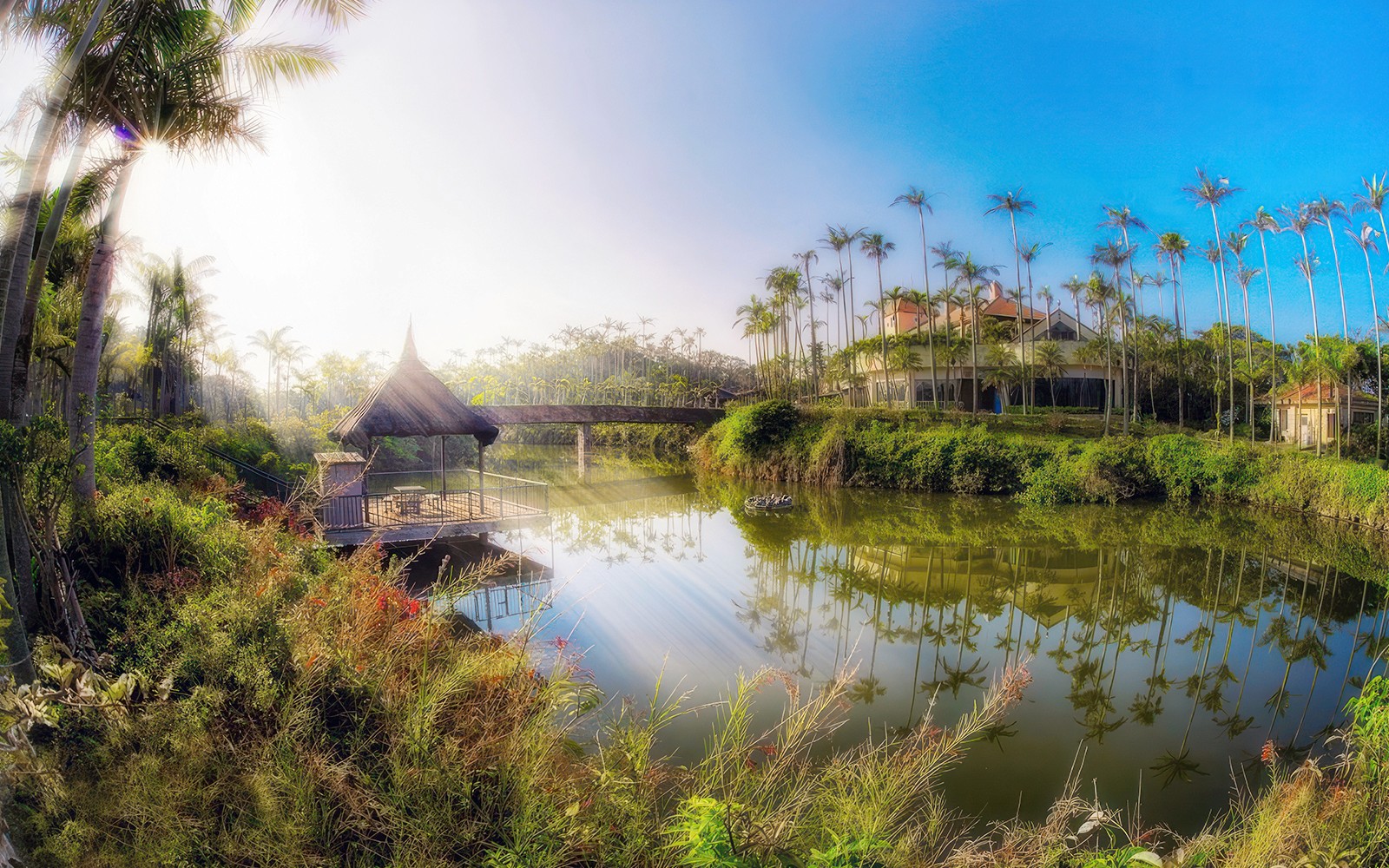 Οι Νοτιοανατολικοί Βοτανικοί Κήποι με φοίνικες και ένα καλύβι από άχυρο δίπλα σε μια γαλήνια λίμνη.