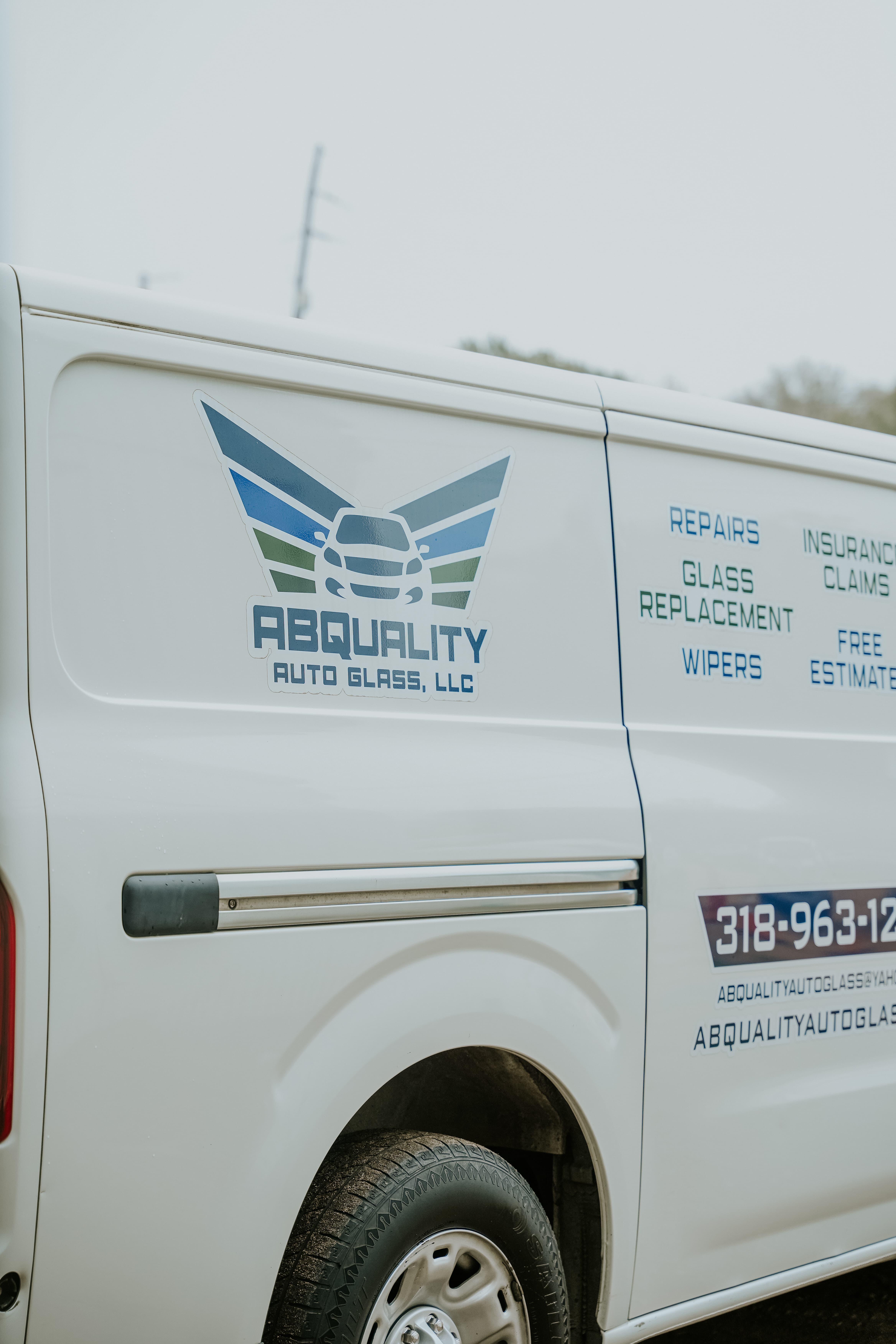 A white van displaying the logo and contact details of Abquality Auto Glass, LLC, featuring services like repairs, glass replacement, insurance claims, and free estimates.