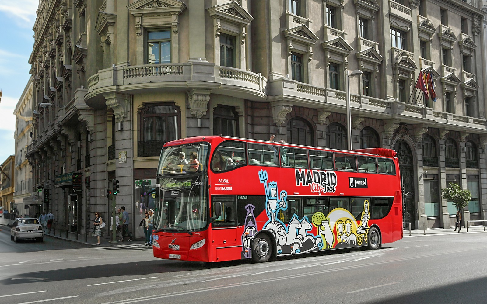 Autobus rosso a due piani del tour della città di Madrid che passa davanti a un edificio storico.