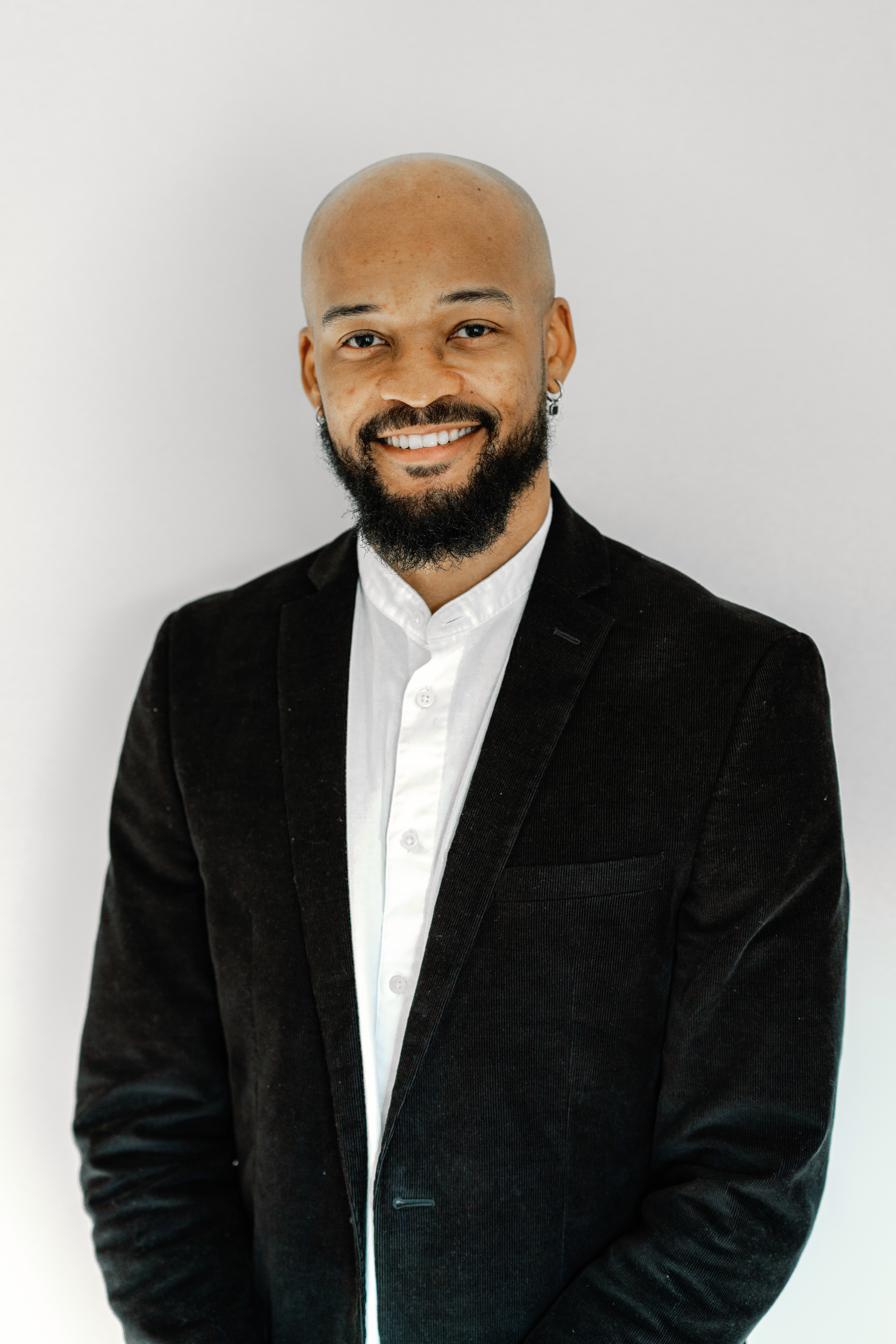 A young person with curly hair smiles at the camera while sitting in front of a laptop against a dark background.