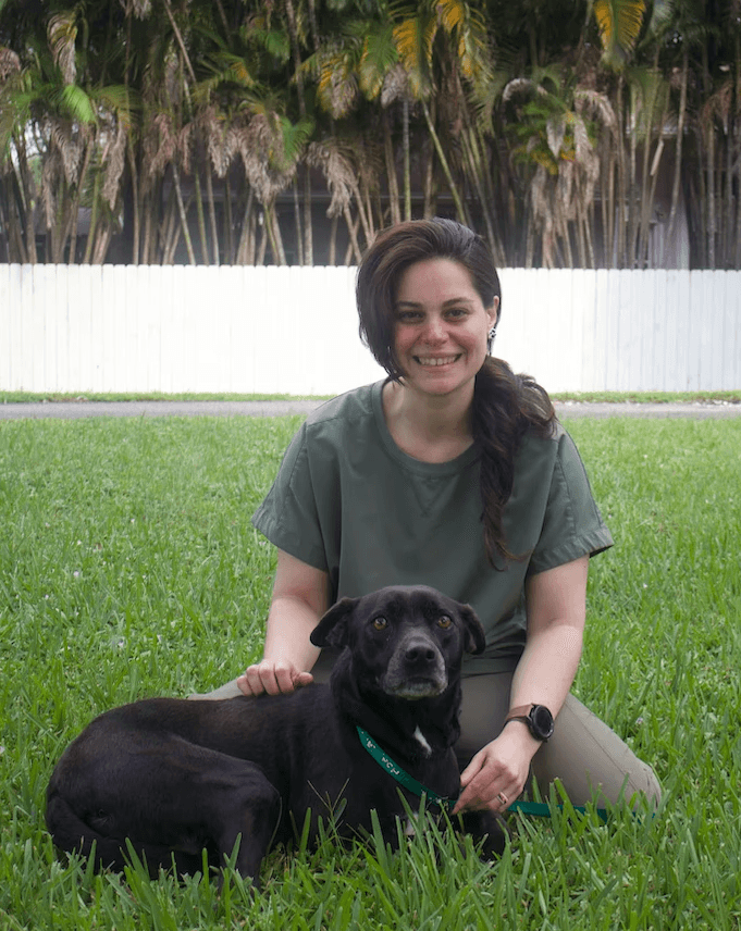 janeline sitting with a black lab mix in the grass