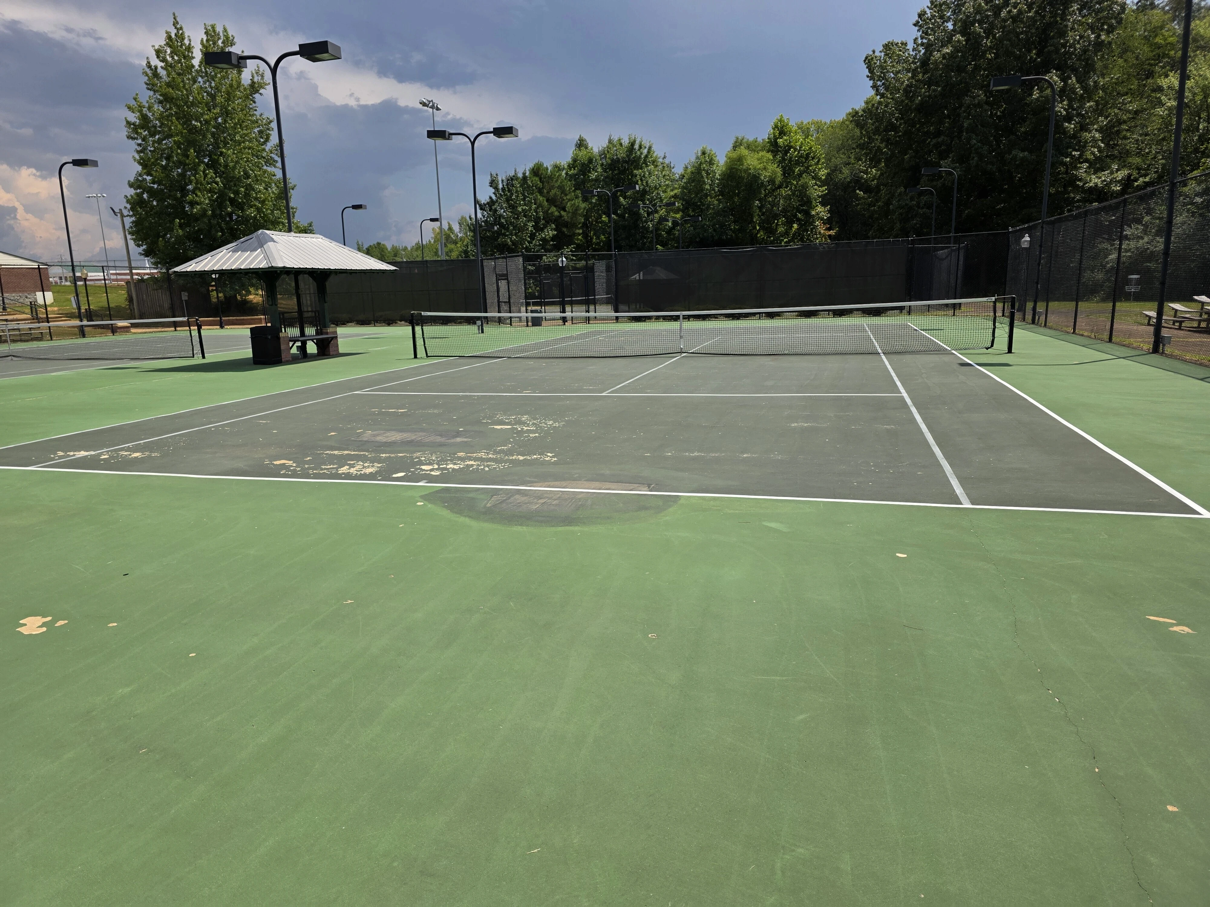 Worn green tennis court with peeling coating and surface damage before resurfacing in Corinth, MS