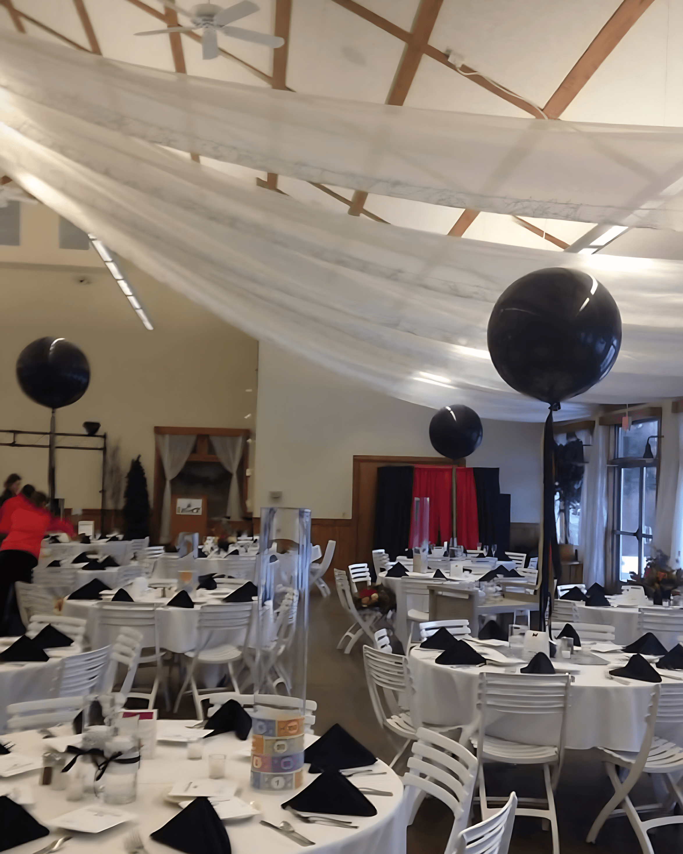 Large event hall decorated with white and black balloon centerpieces and hanging drapes for a formal gathering by Be Bold Balloons