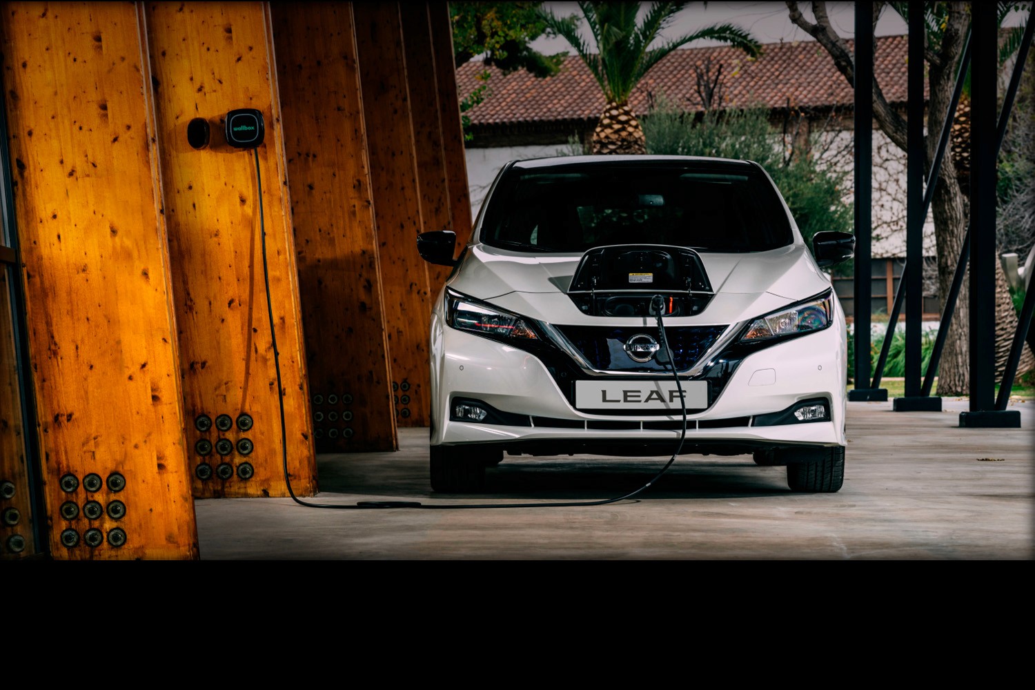 "Técnico de Citroën sonriendo mientras revisa un vehículo blanco con detalles rojos, en un taller con neumáticos al fondo."