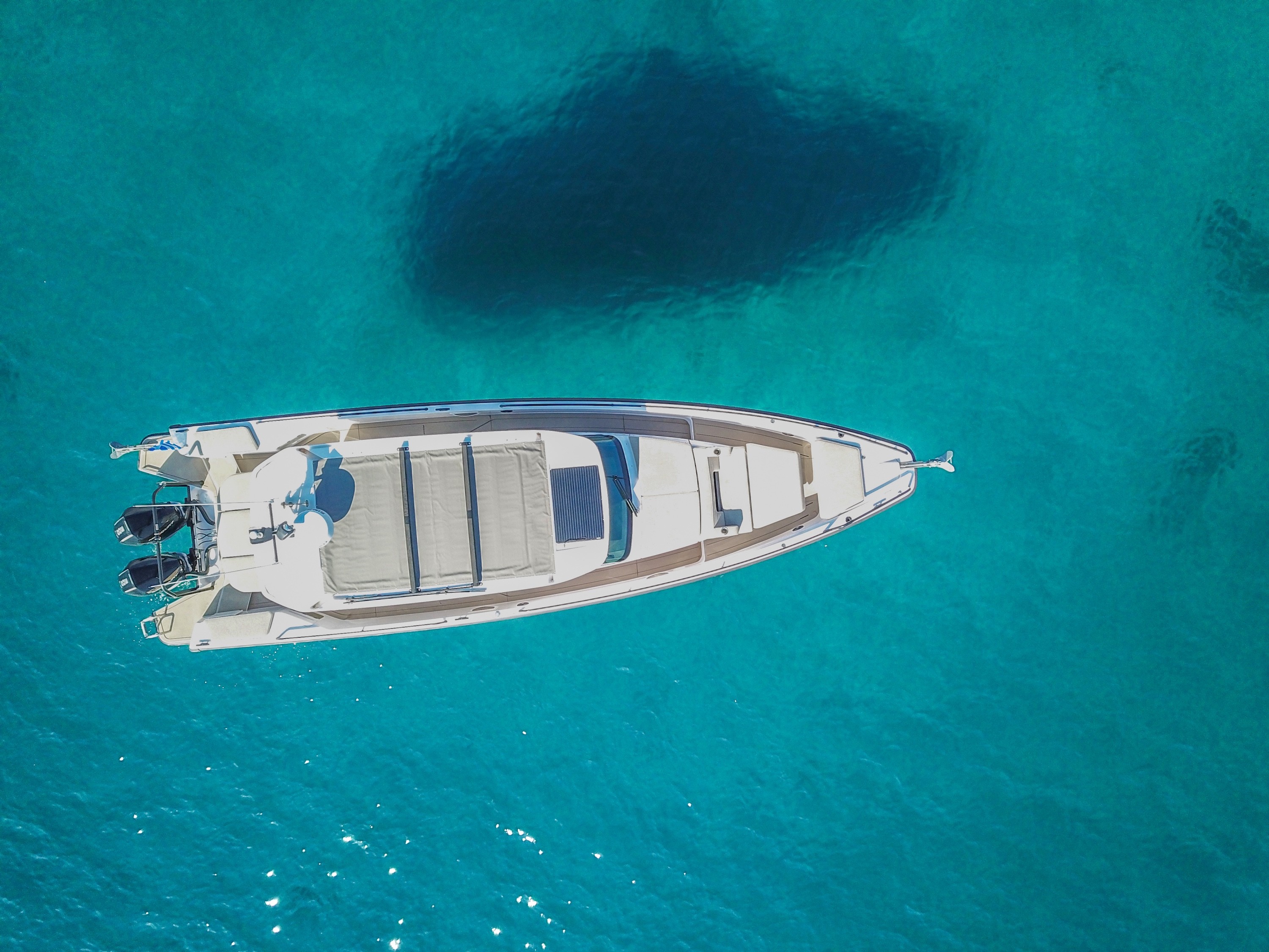 White Axopar 37 Zeus motor yacht anchored in crystal-clear turquoise waters, aerial view showing underwater rock formations beneath.